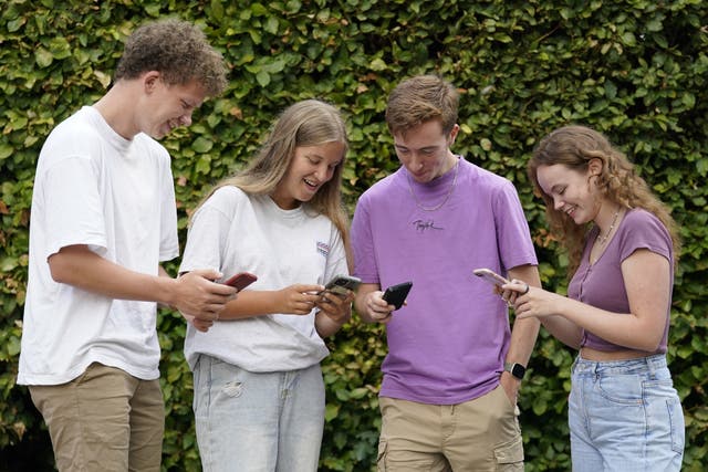 Students Ben Surtees, Bryony Lucas, James McSaprron and Leonie Rowe check their results on their phones at Peter Symonds College, Winchester, Hampshire (Andrew Matthews/PA)