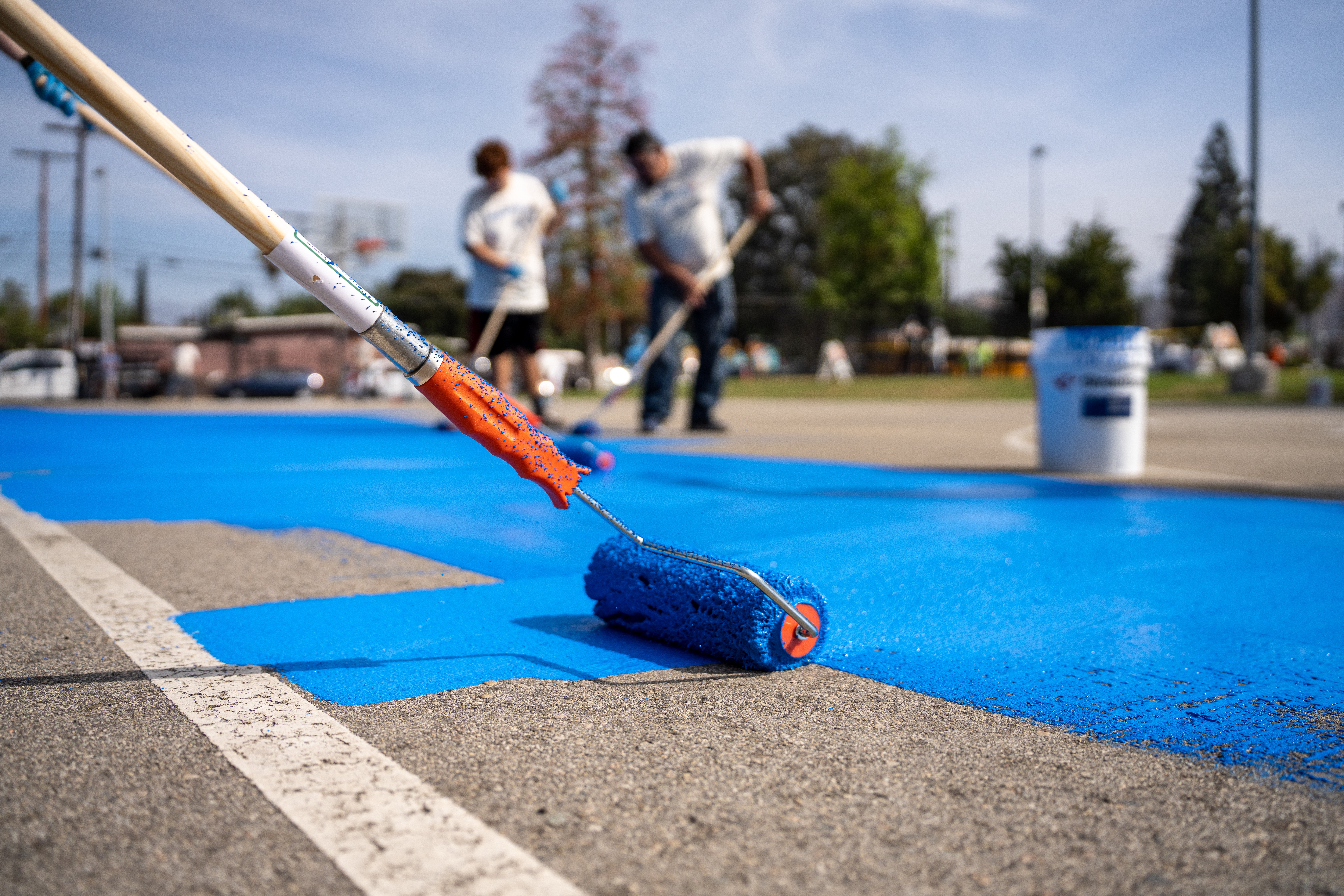 Light- and heat-reflecting paint is rolled onto a basketball court in Los Angeles