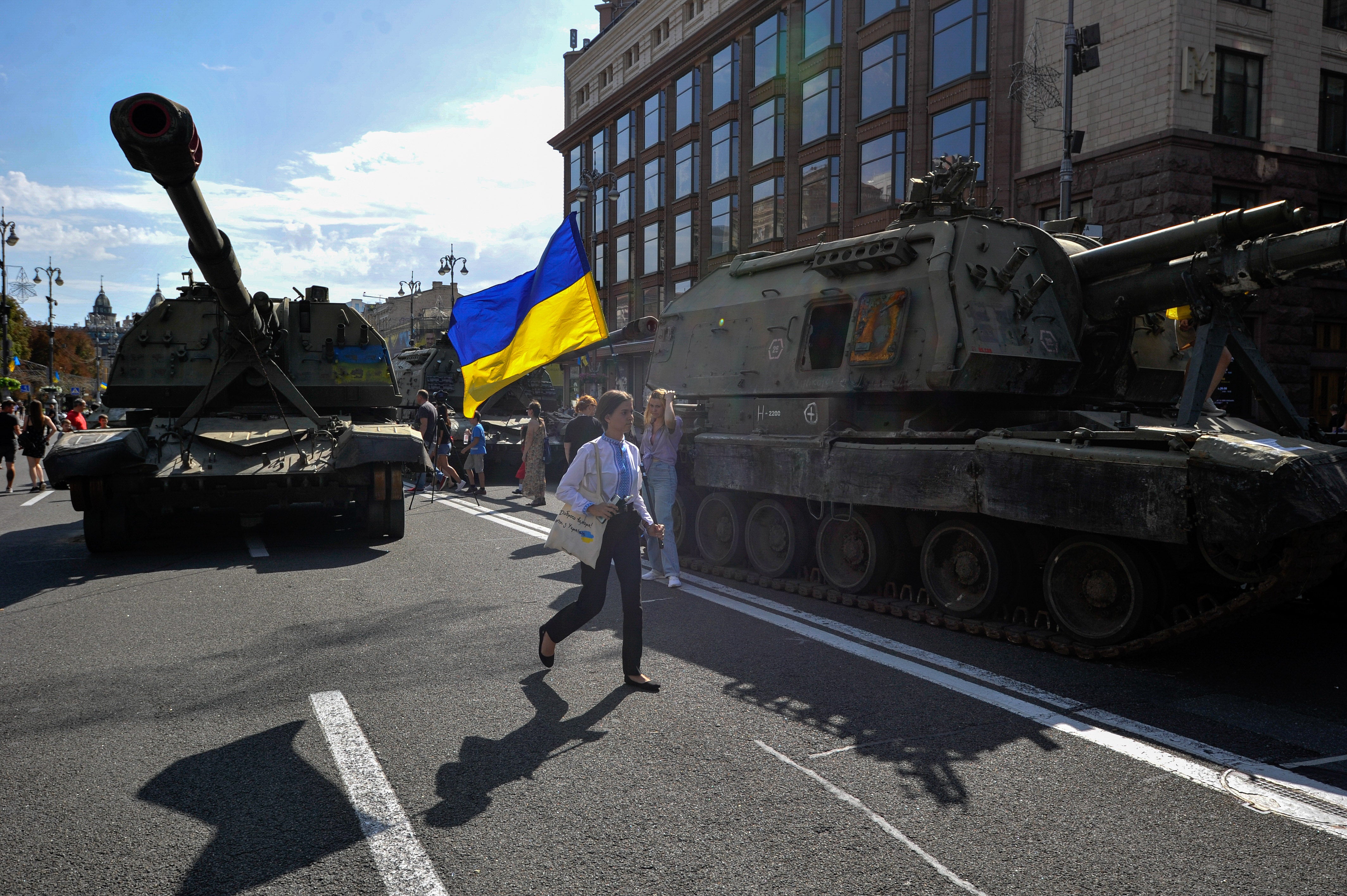 A young girl holds a Ukrainian flag next to destroyed Russian military hardware in Kyiv on 24 August, 2022.
