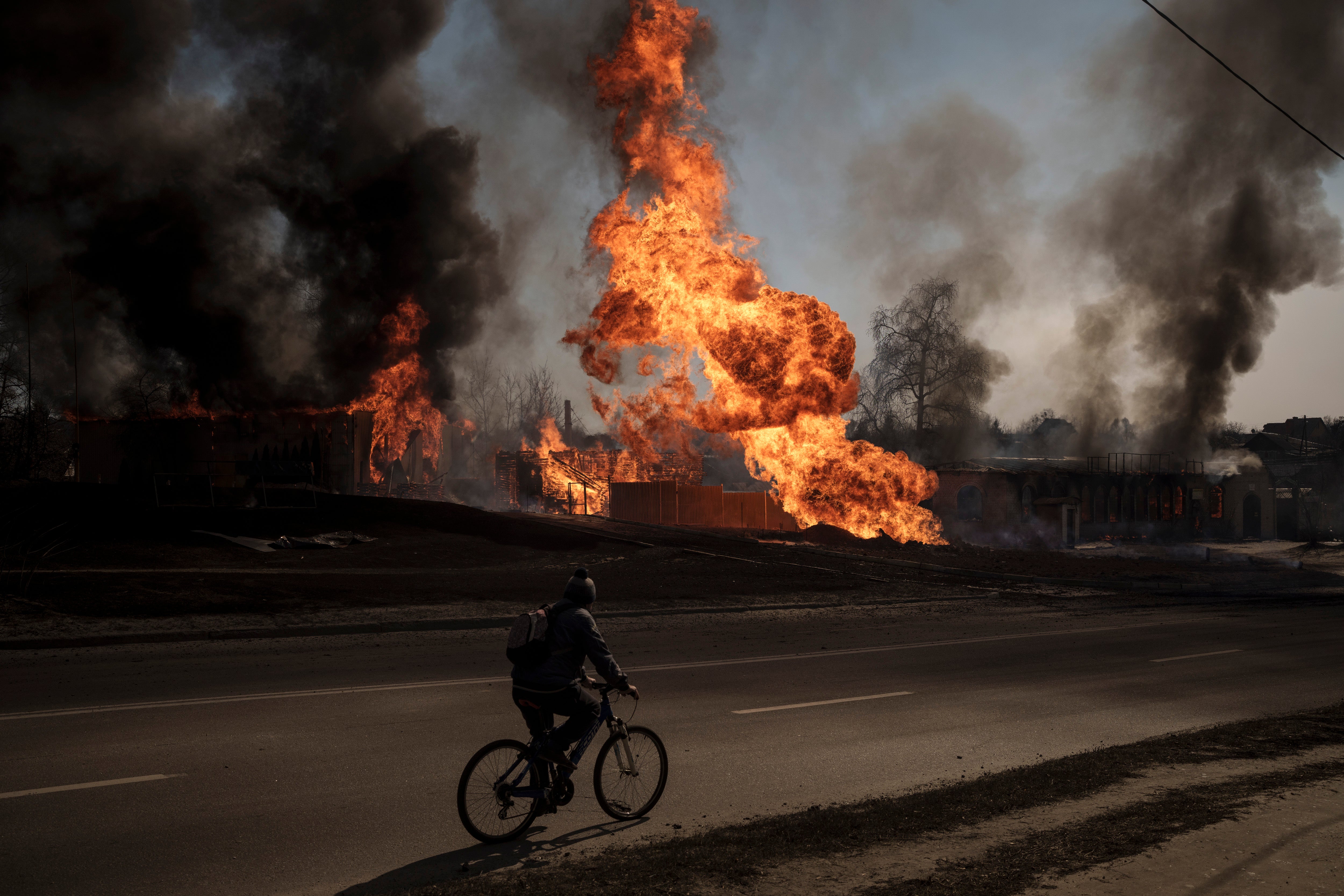 A man cycles past flames after a Russian attack in Kharkiv on 25 March, 2022.