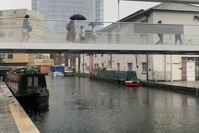 Commuters shelter under umbrellas while crossing a bridge over the canal in Paddington, west London (Peter Clifton/PA)
