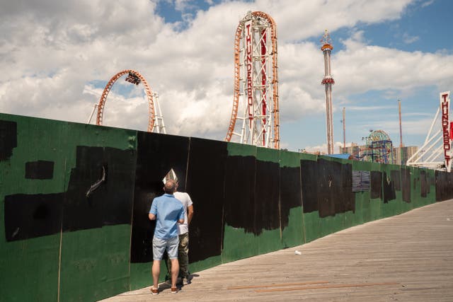 <p>(Representative) People watch a  rollercoaster through an opening on partitions of a construction site at Coney Island beach on 4 July 2021 in New York City</p>