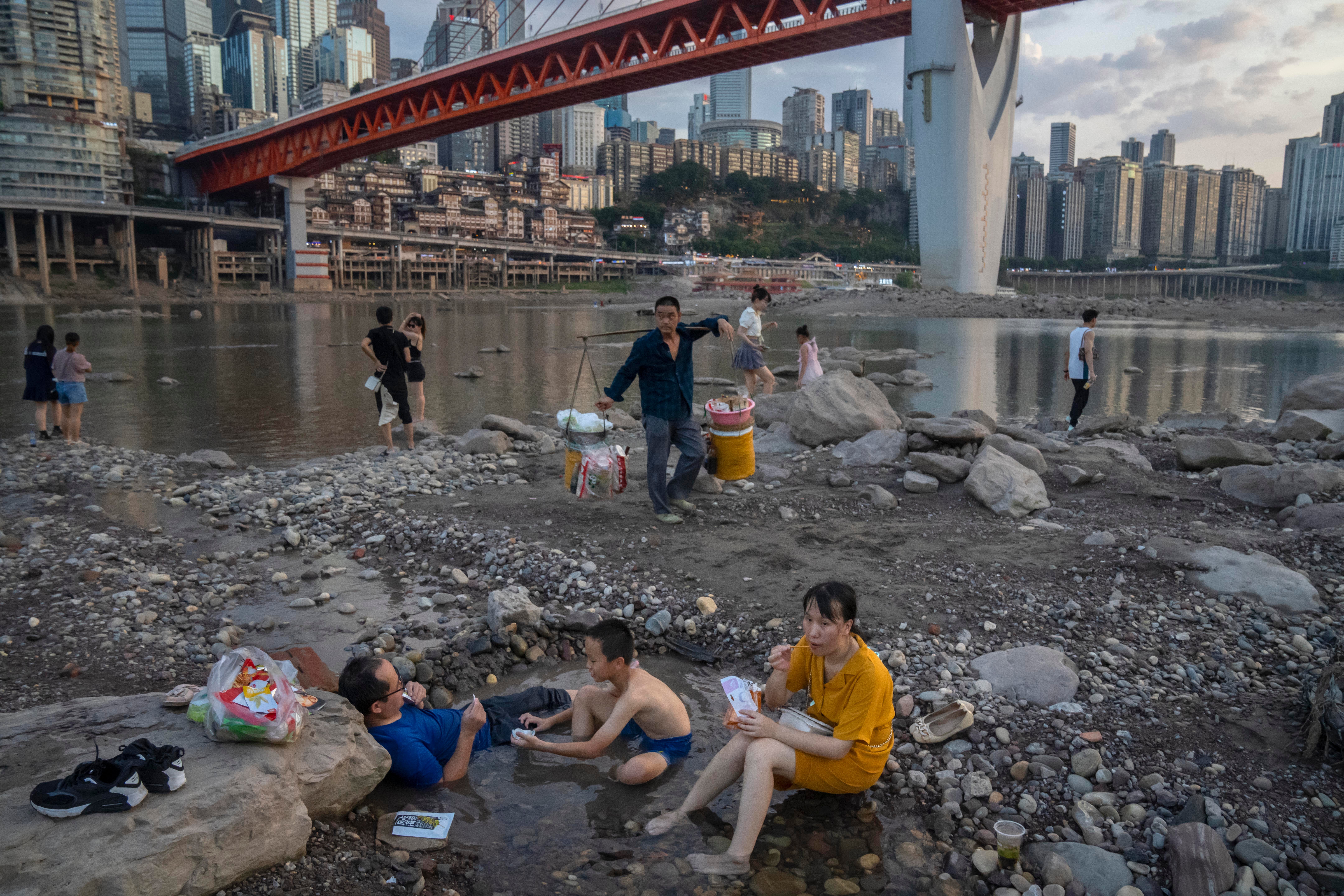 People sit in a shallow pool of water in the riverbed of the Jialing River, a tributary of the Yangtze, in southwestern China's Chongqing Municipality