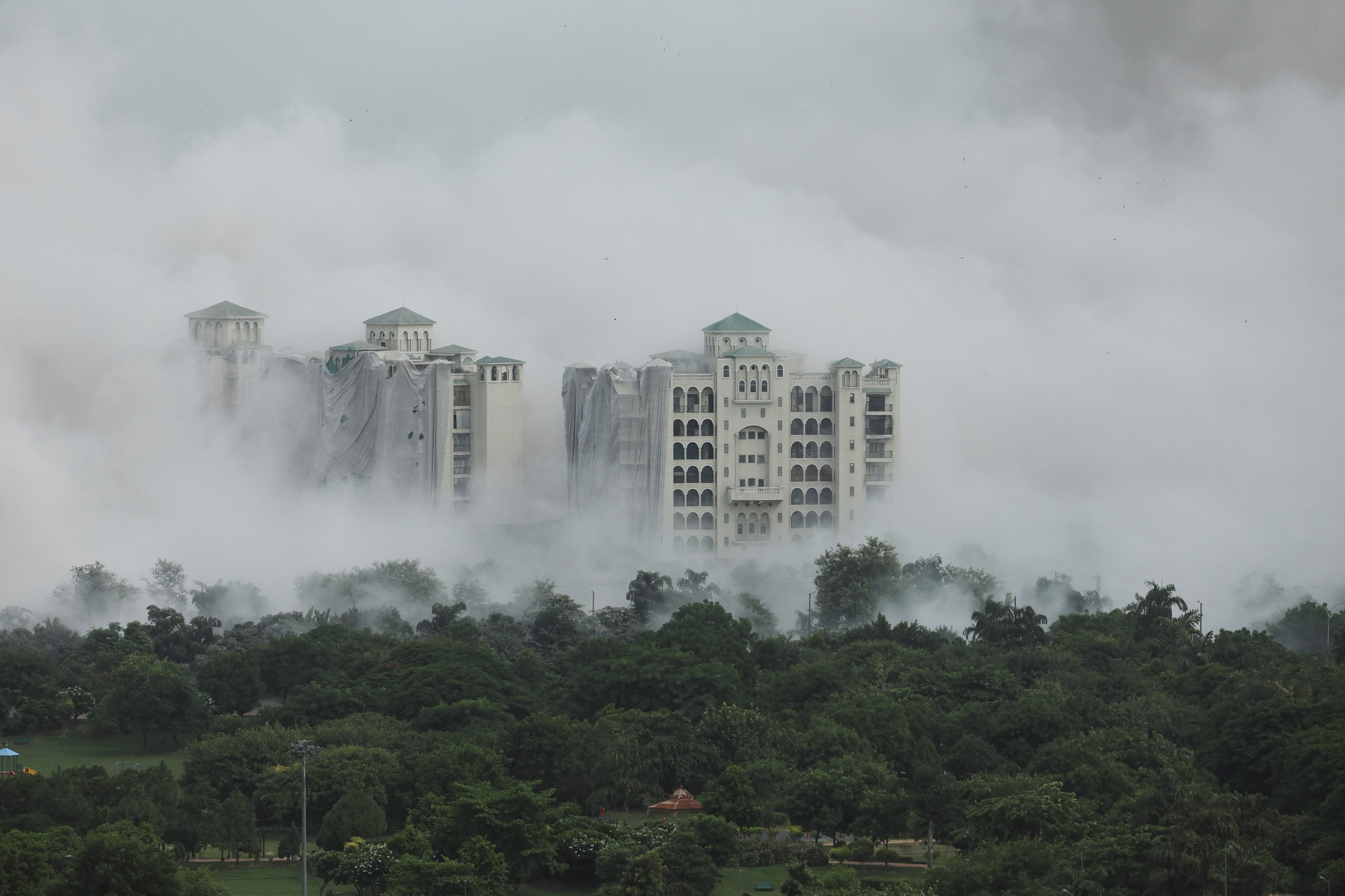 Dust plume engulfs surrounding buildings after controlled demolition
