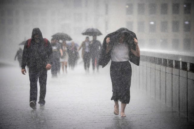 <p>People cross London Bridge during heavy rainfall on 17 August 2022</p>