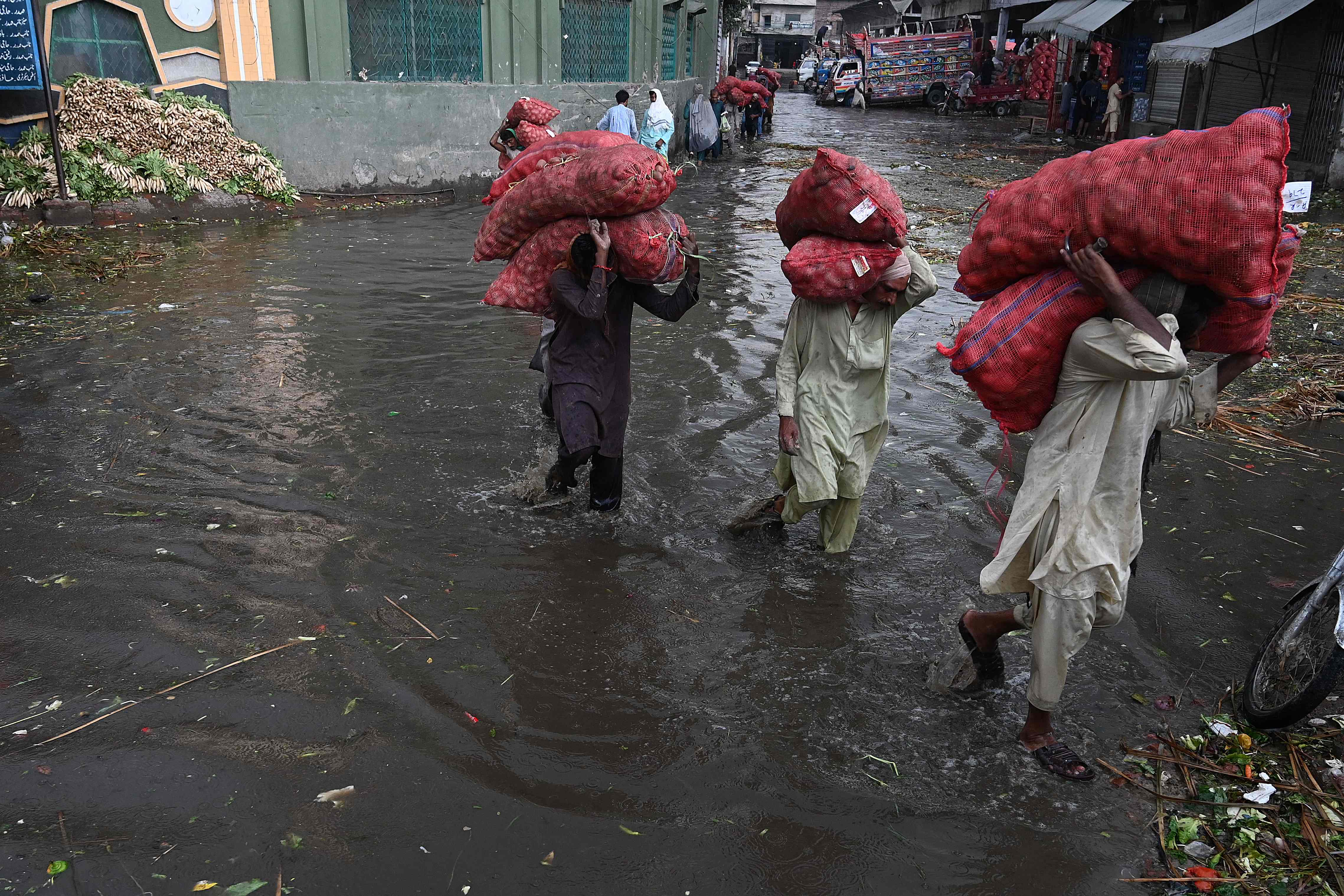 Labourers carry sacks of potato as they wade amid a flooded market in Lahore