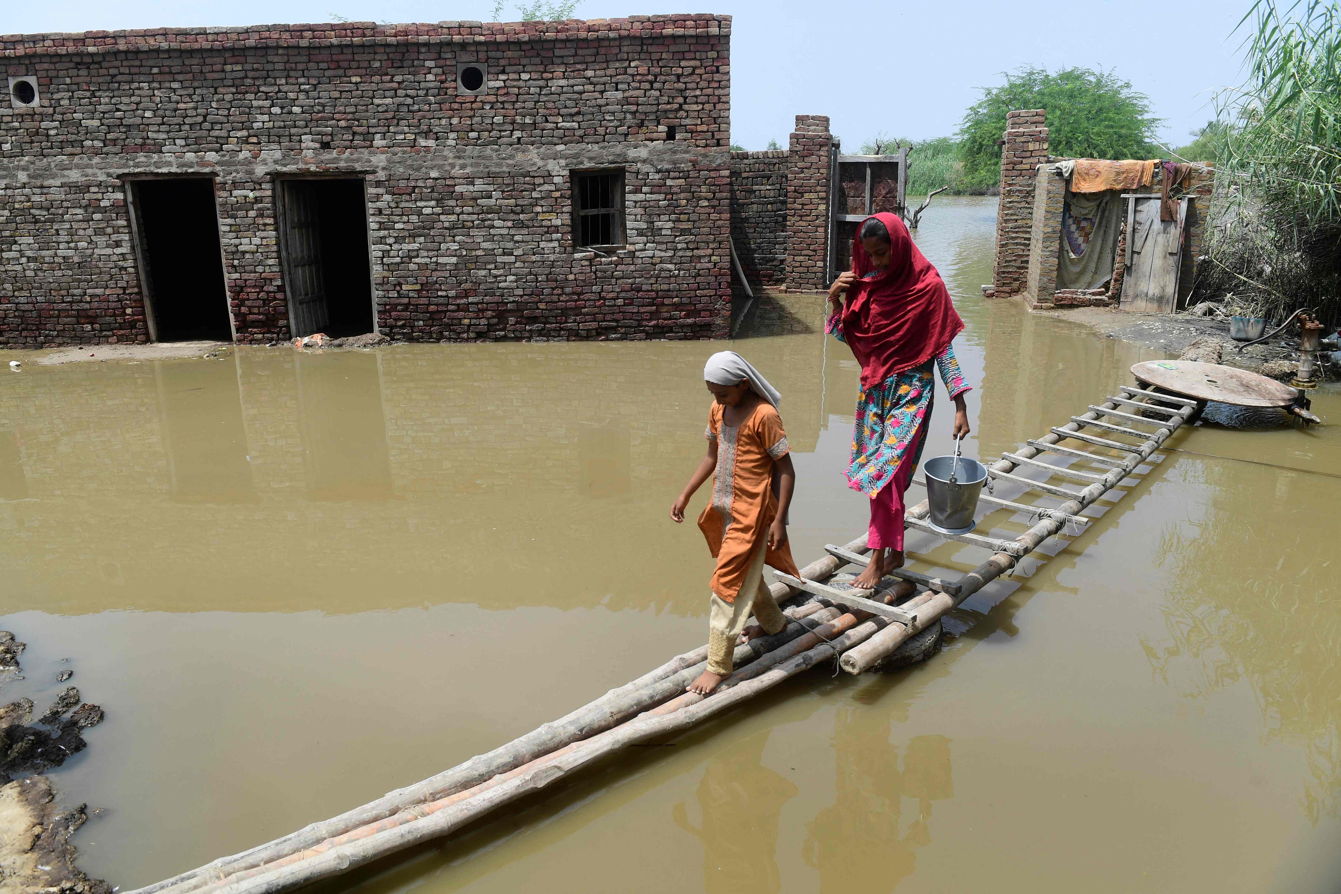 Two women cross a temporary bamboo path near their flooded house in Shikarpur of Sindh province on Monday