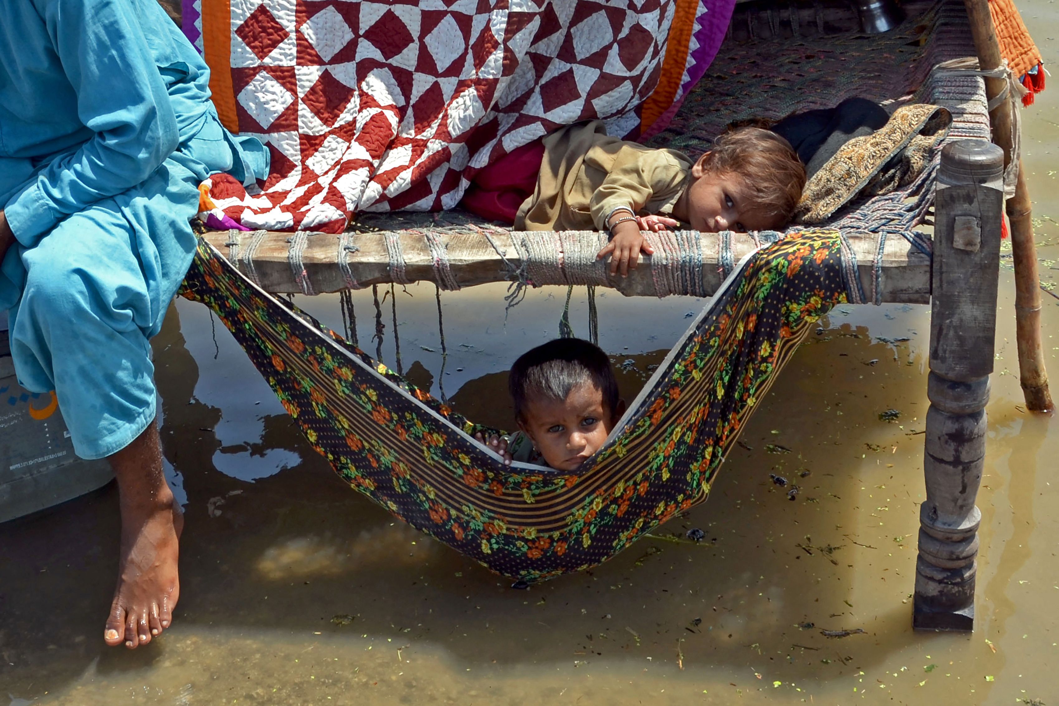 Flood-affected children sit on a traditional cot alongside flood waters after heavy monsoon rains in the Jaffarabad district of Balochistan province on 31 August