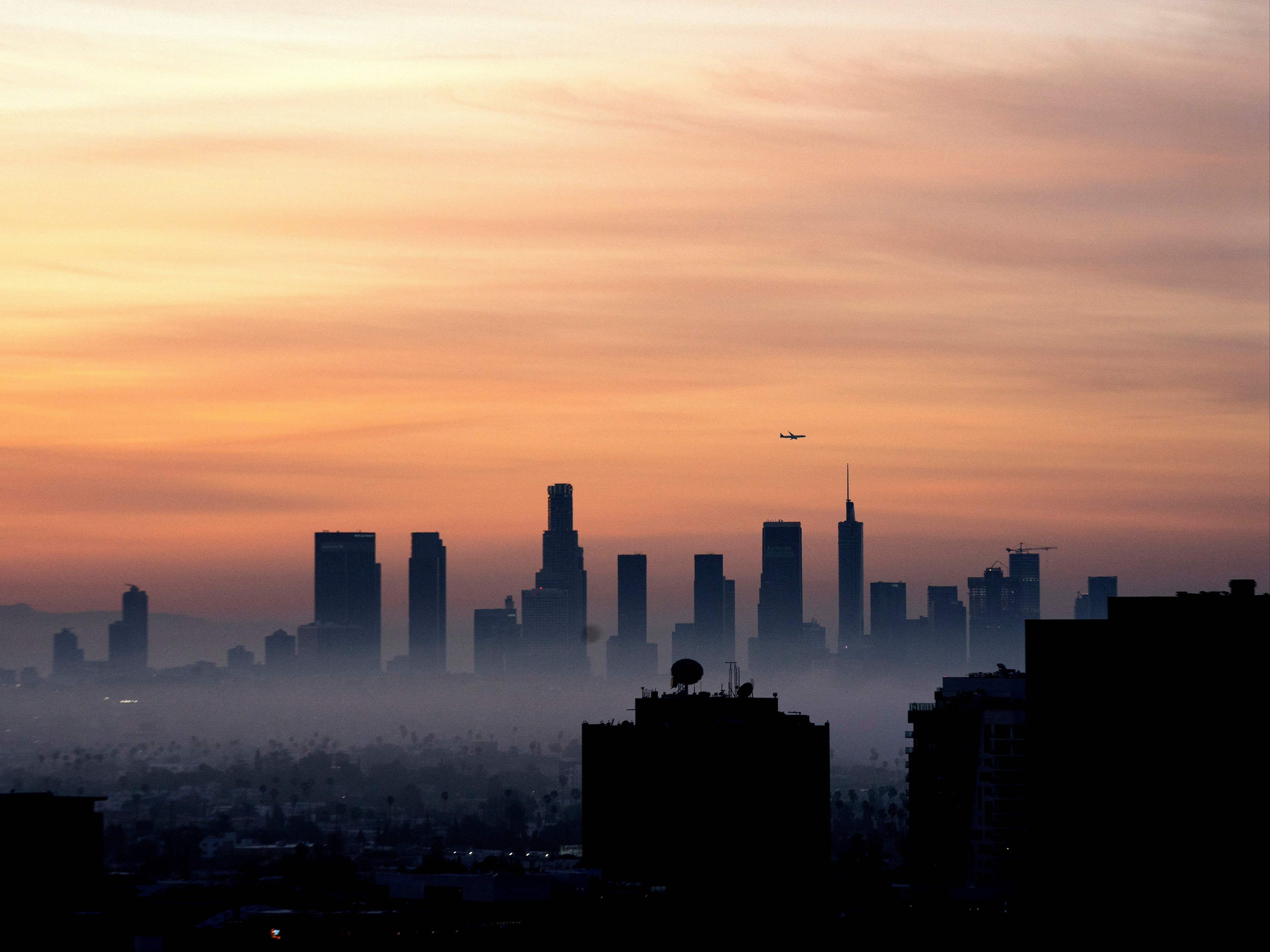 <p>A plane flies over the Los Angeles, California, skyline at sunrise on March 25, 2022</p>