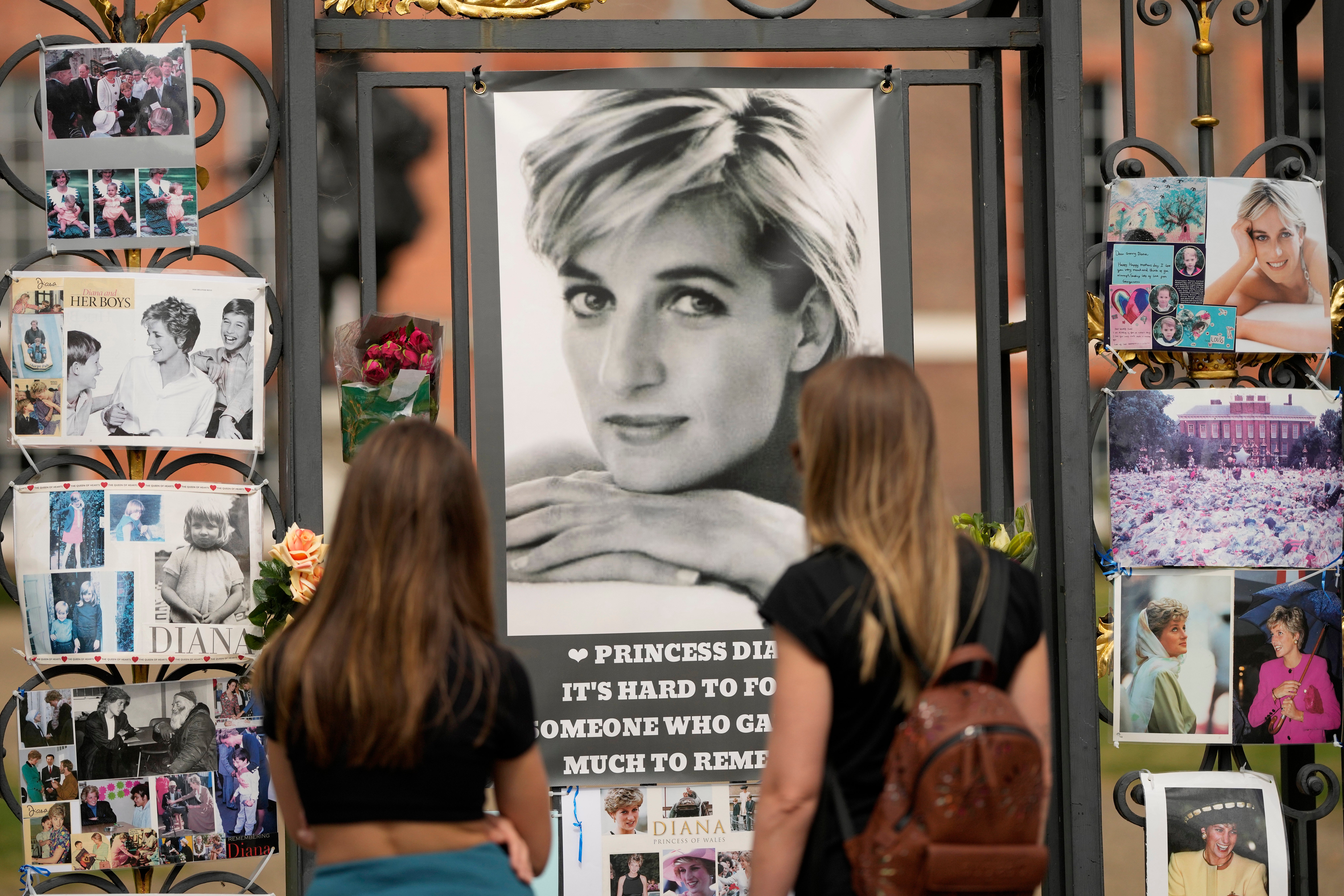 Two women look at portraits of Princess Diana and other remembrances displayed on the gates of Kensington Palace