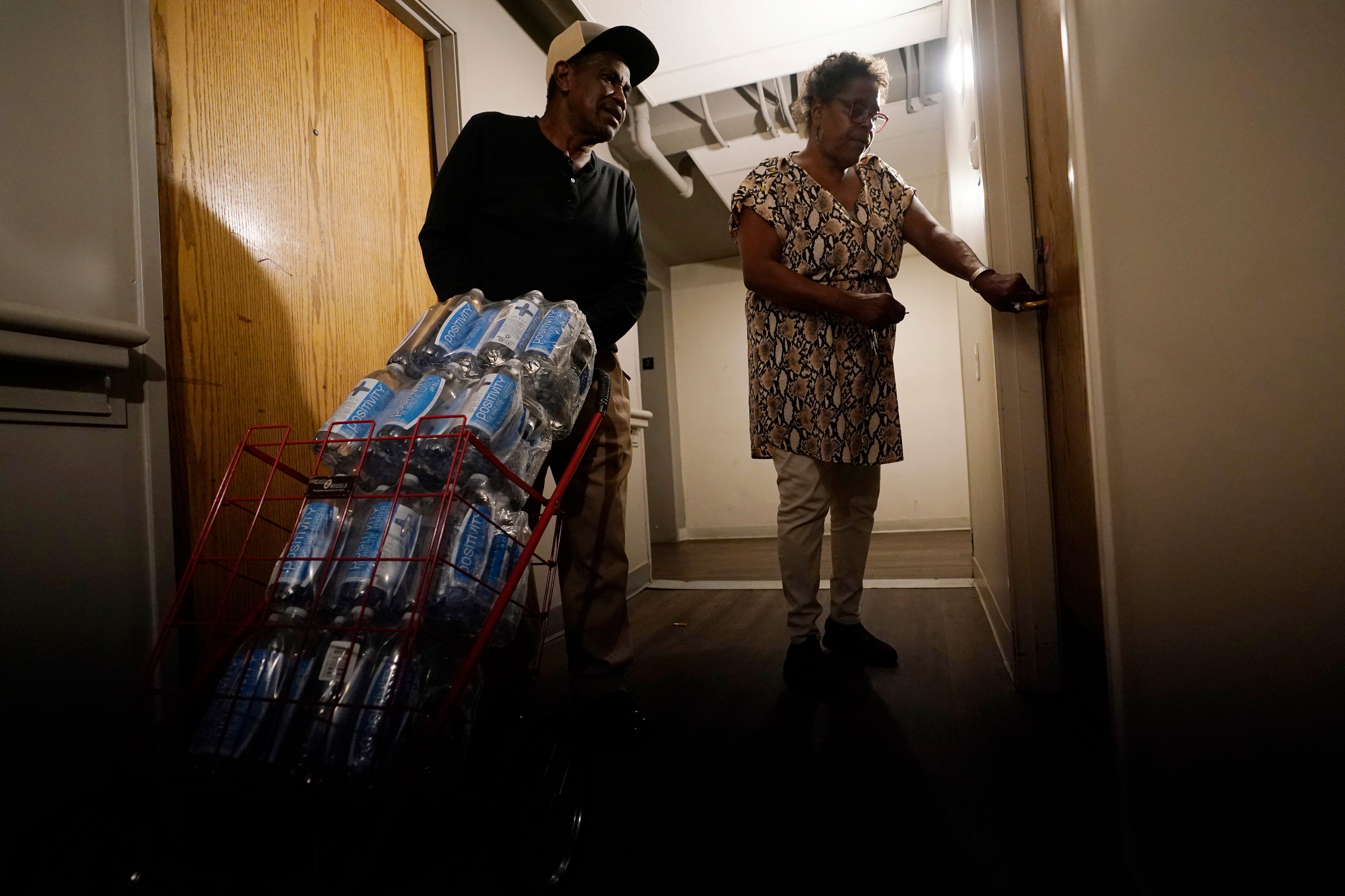 Mary Gaines, right, a resident of the Golden Keys Senior Living apartments, unlocks her door as a friend helps her with cases of fresh water in Jackson