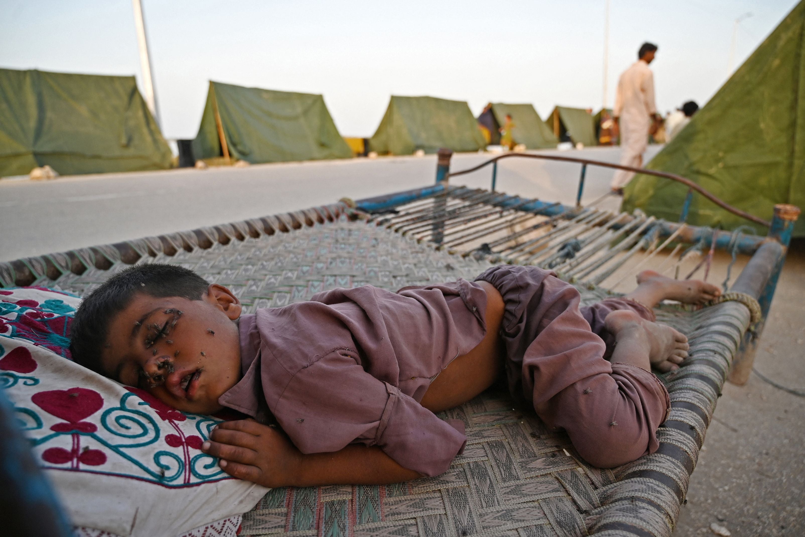 Houseflies sit on the face of a boy sleeping outside his tent at a makeshift camp after heavy monsoon rains in Sukkur, Sindh