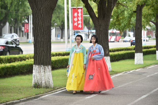 <p>Two women wear traditional hanbok dresses as they walk on a street in Pyongyang</p>