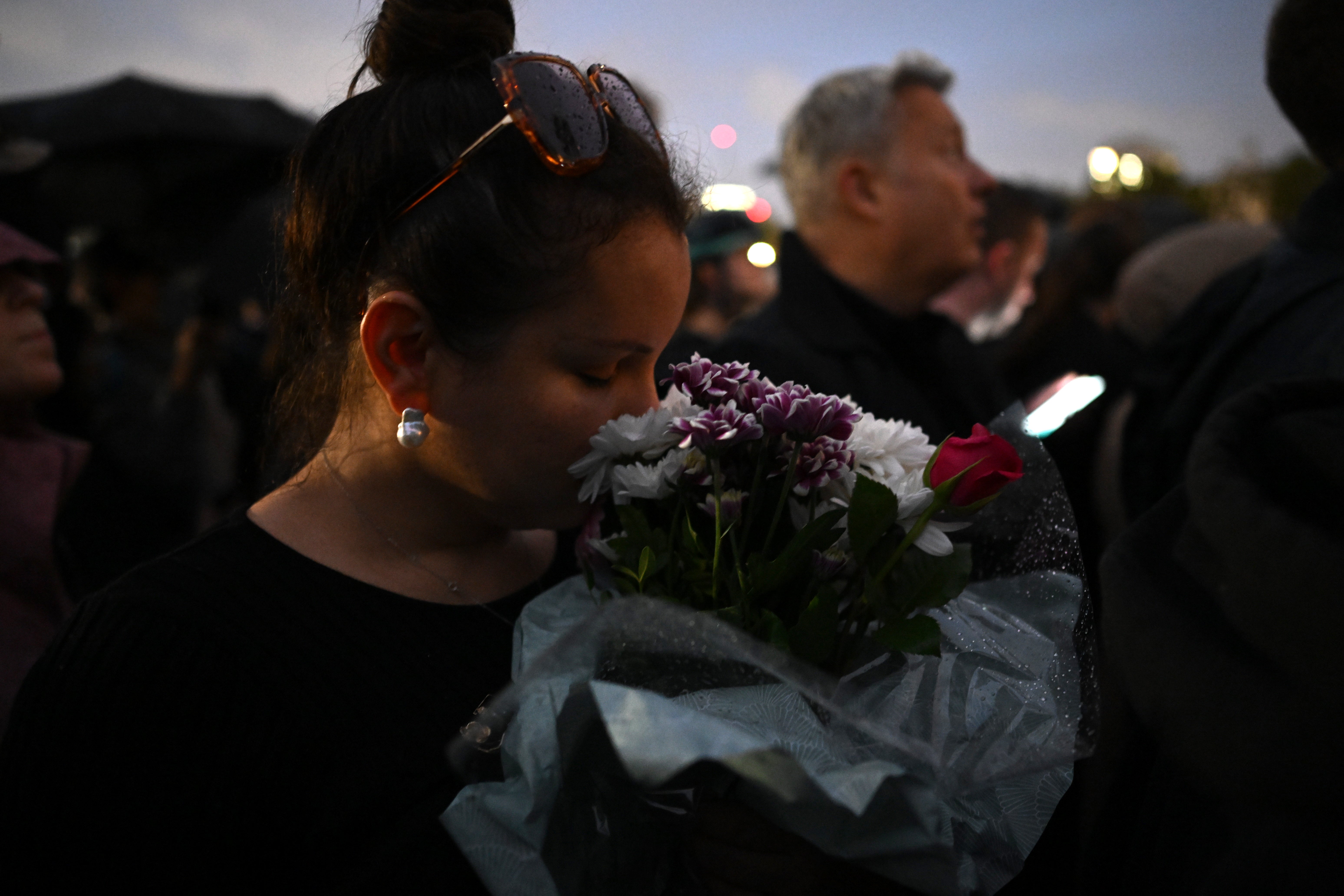 A woman holds a bouquet of flowers, as crowds gather in front of Buckingham Palace