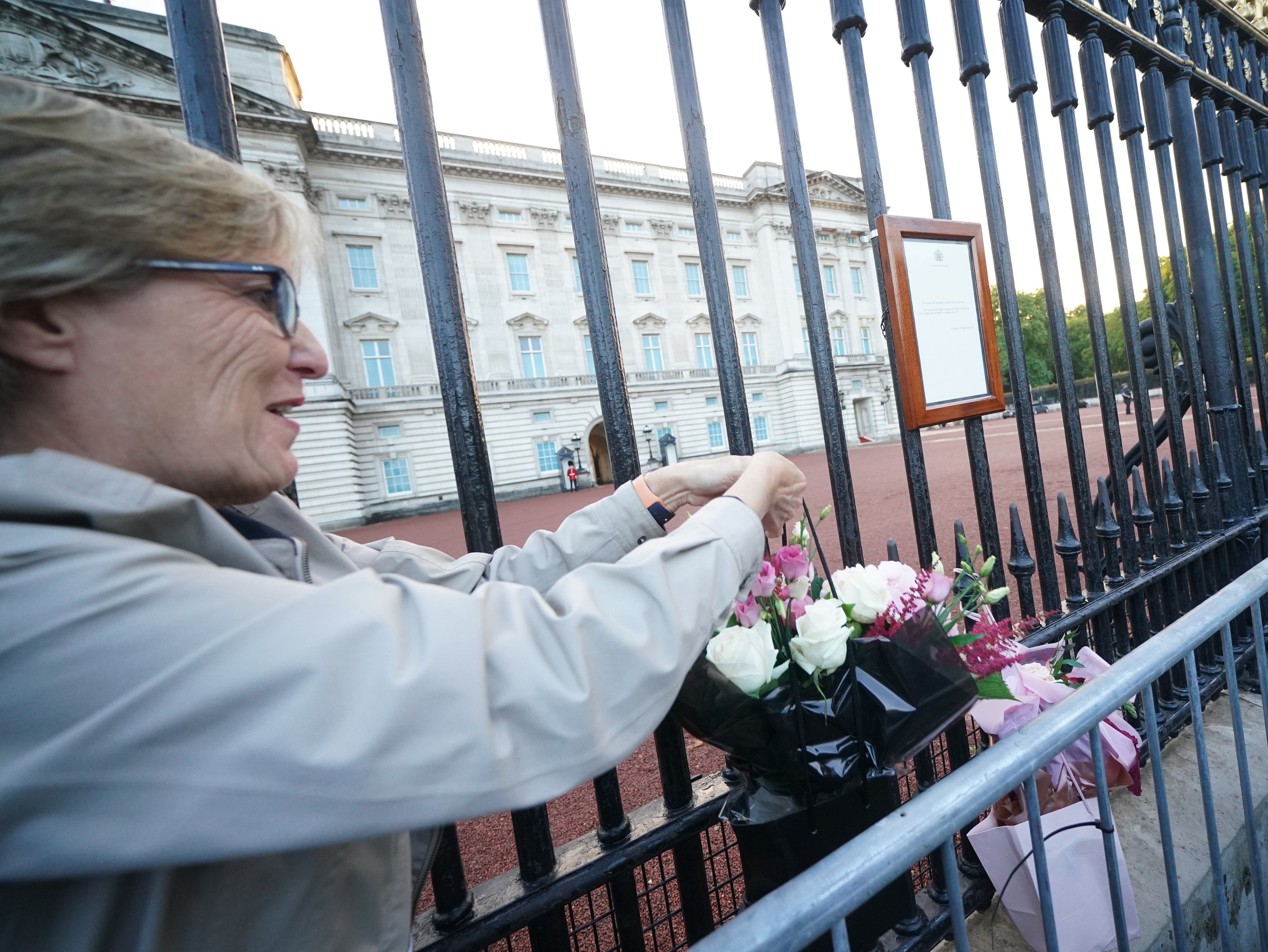 A woman ties flowers to the gates at Buckingham Palace announcing the Queen’s death (Yui Mok/PA)
