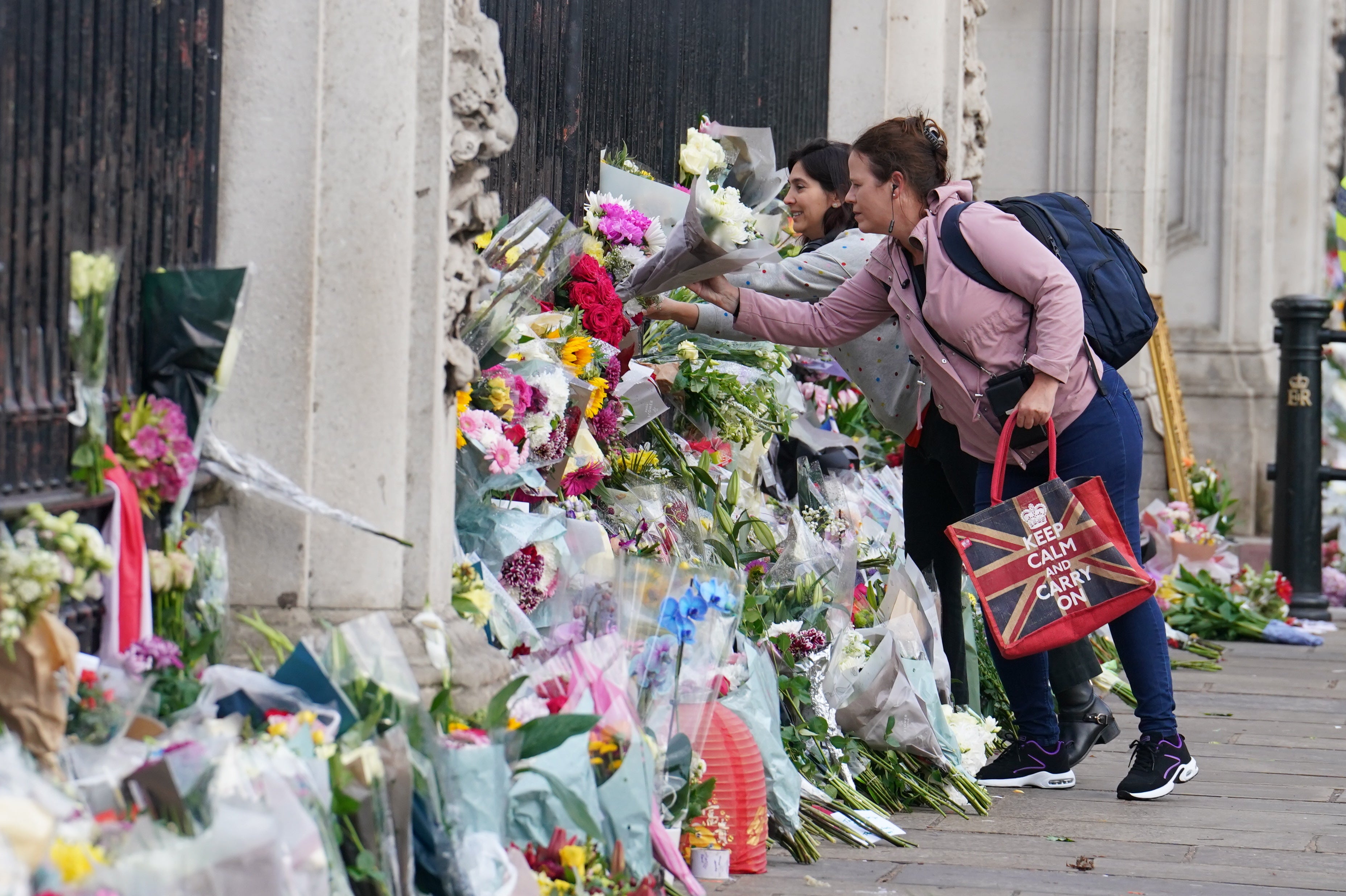 A woman lays flowers by the railings at Buckingham Palace (Dominic Lipinski/PA)