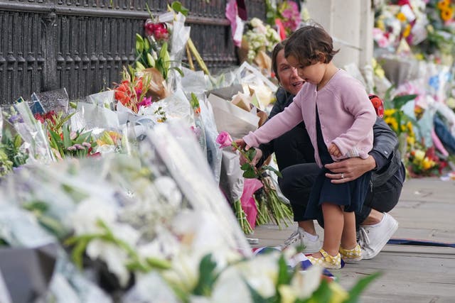 A woman and a child lay a single pink rose by the railings at Buckingham Palace (Dominic Lipinski/PA)