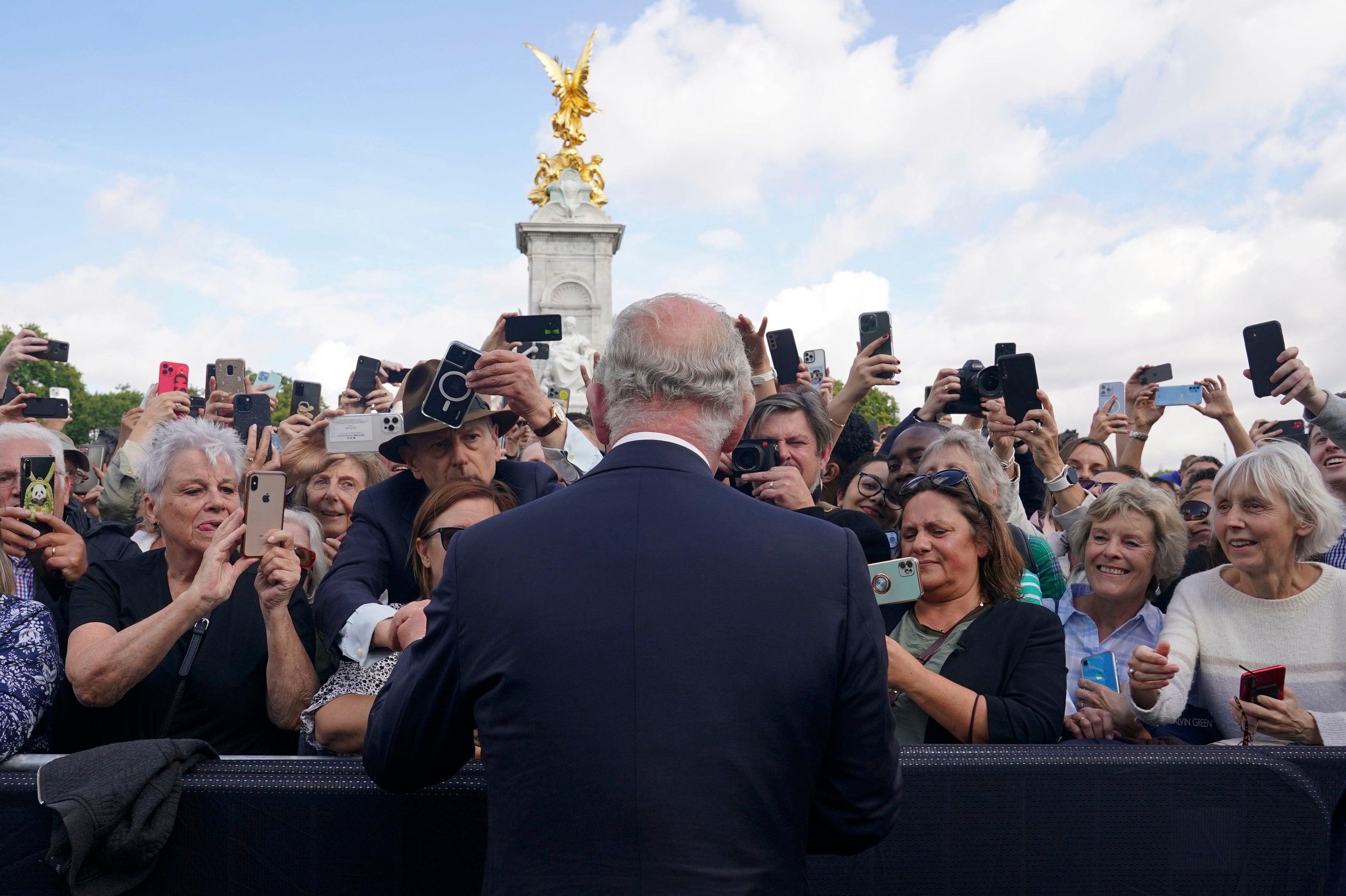 The King greets well-wishers as he walks by the gates of Buckingham Palace on Friday