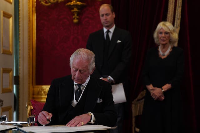 King Charles III signs an oath to uphold the security of the Church in Scotland during the Accession Council at St James’s Palace watched by his wife and elder son (Victoria Jones/PA)