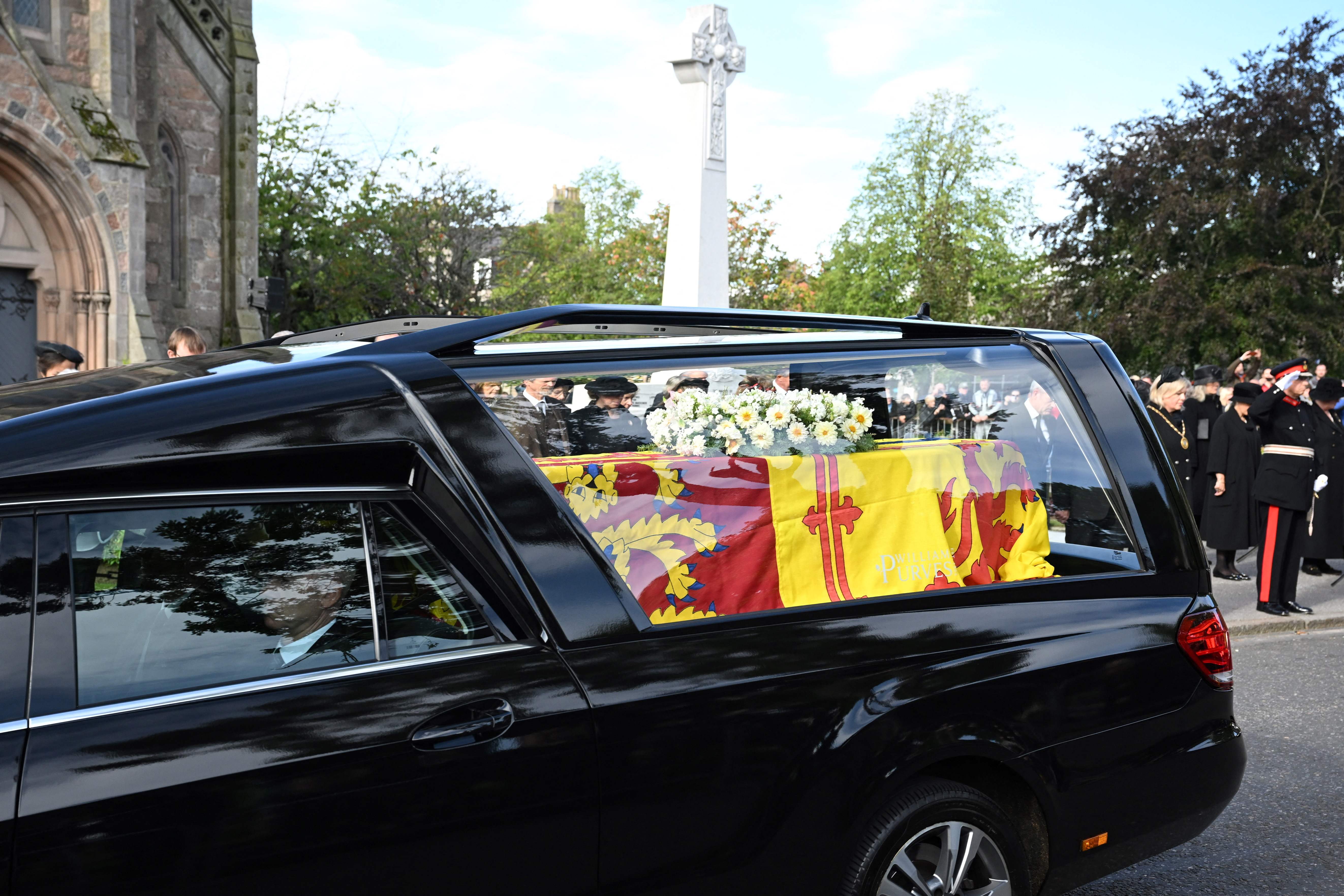 Members of the Public pay their respects as the hearse carrying the coffin of Queen Elizabeth II, draped in the Royal Standard of Scotland, is driven through Ballater