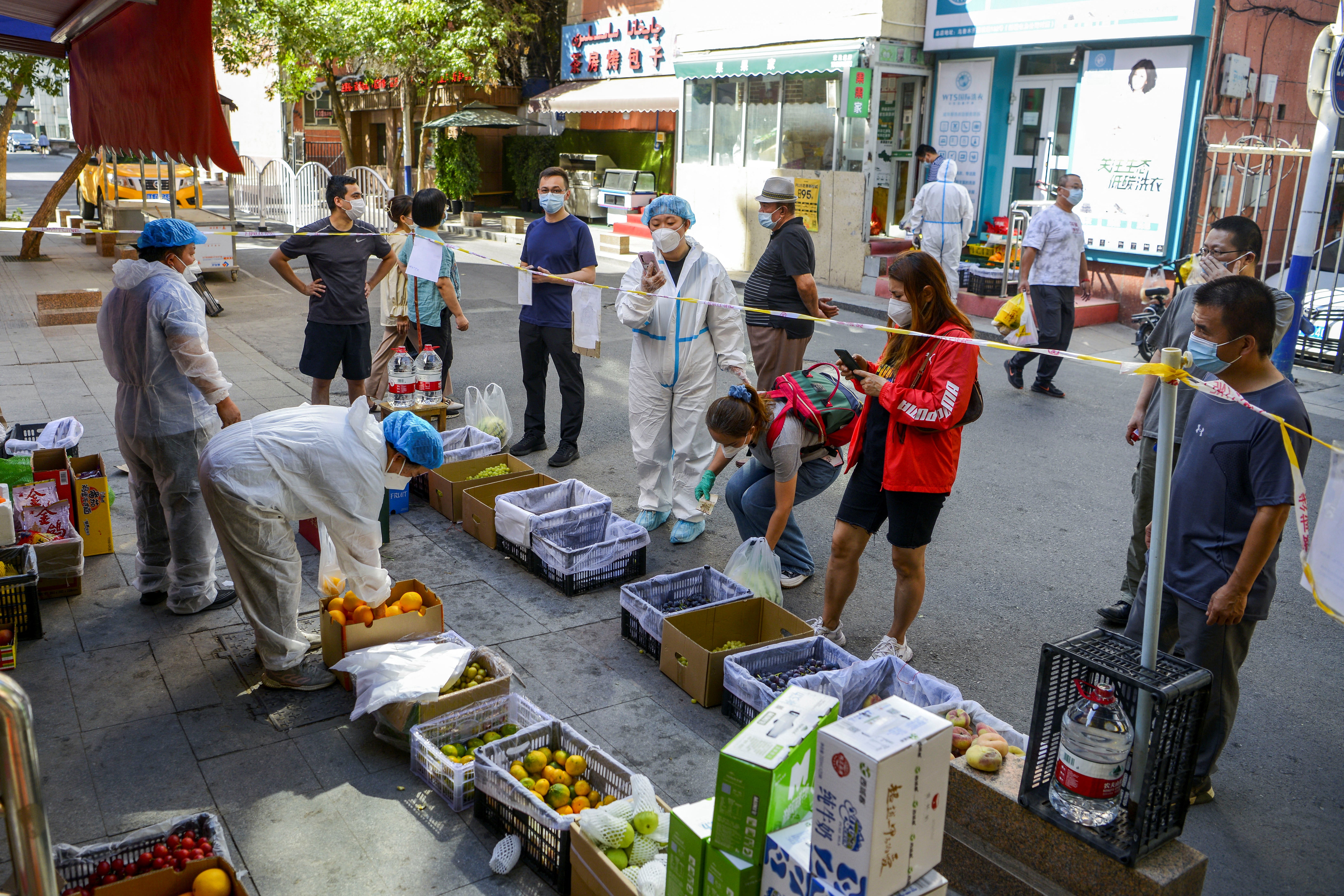 <p>Residents stand behind a cordon line shop at a fruit stall in Xinjiang</p>