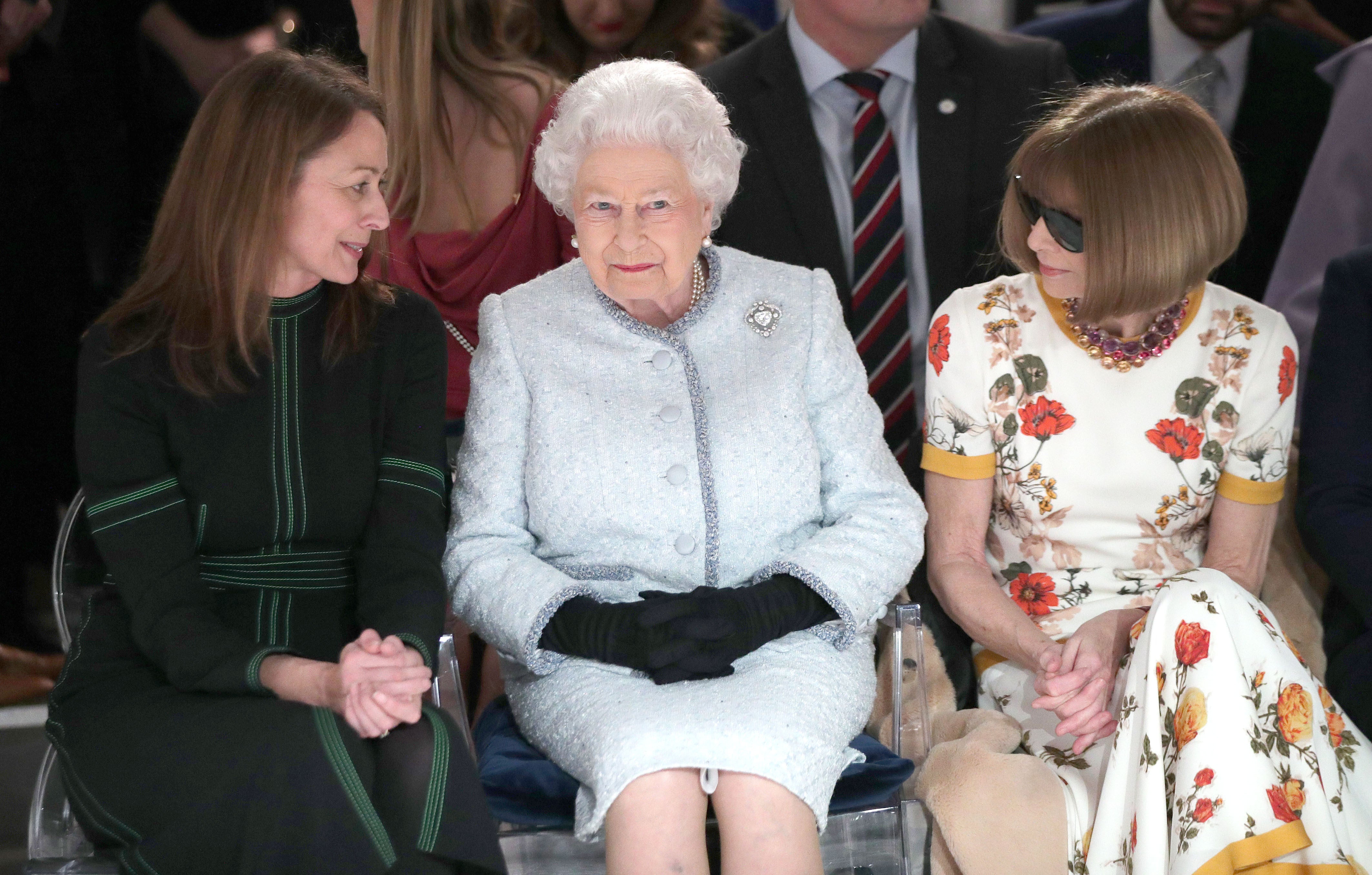 The Queen sits next to Caroline Rush, chief executive of the British Fashion Council, left, and Anna Wintour, right, as they view Richard Quinn’s runway show (Yui Mok/PA)