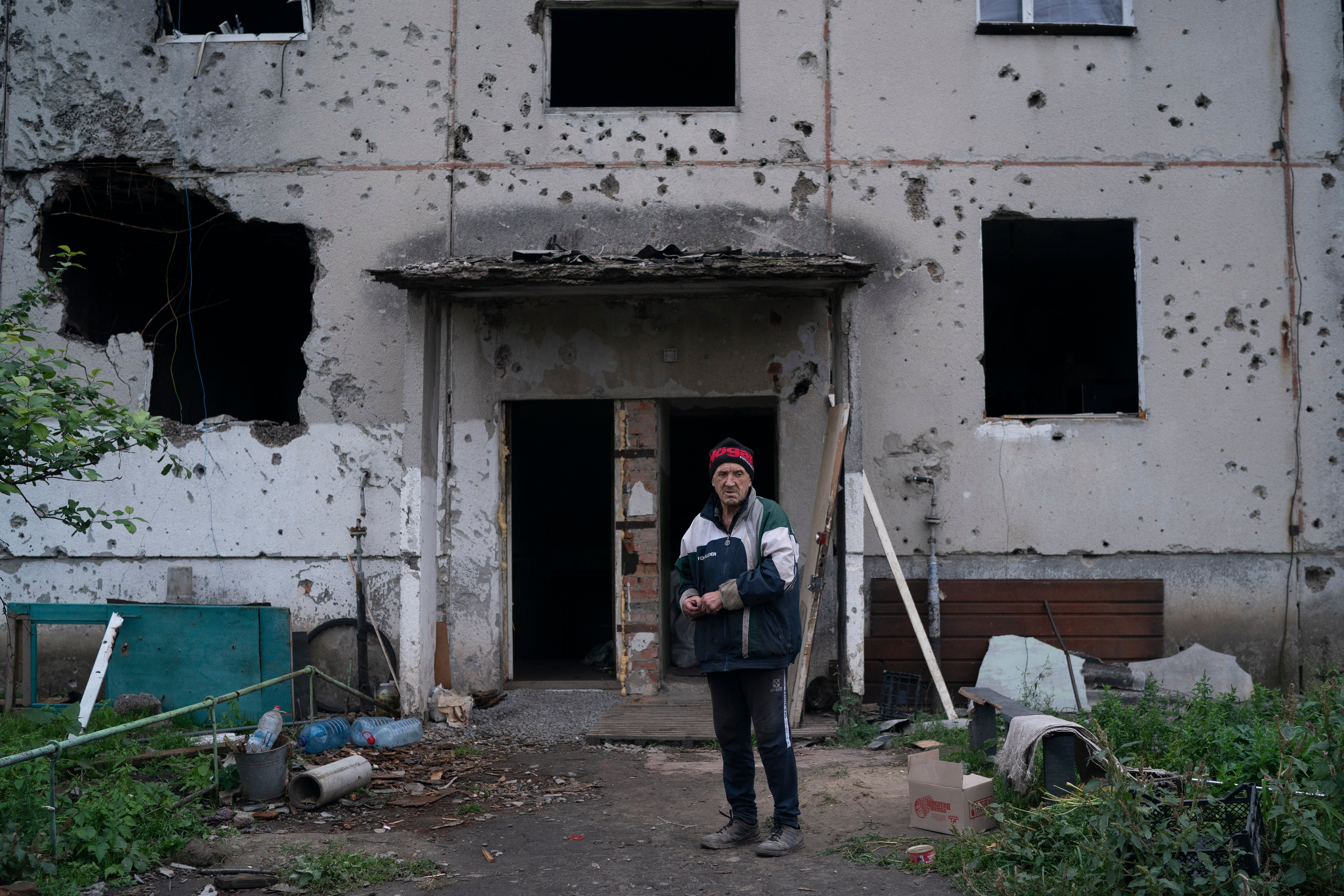 Oleh Lutsai, 70, stands in front of the entrance of the damaged building where he lives in the freed village of Hrakove