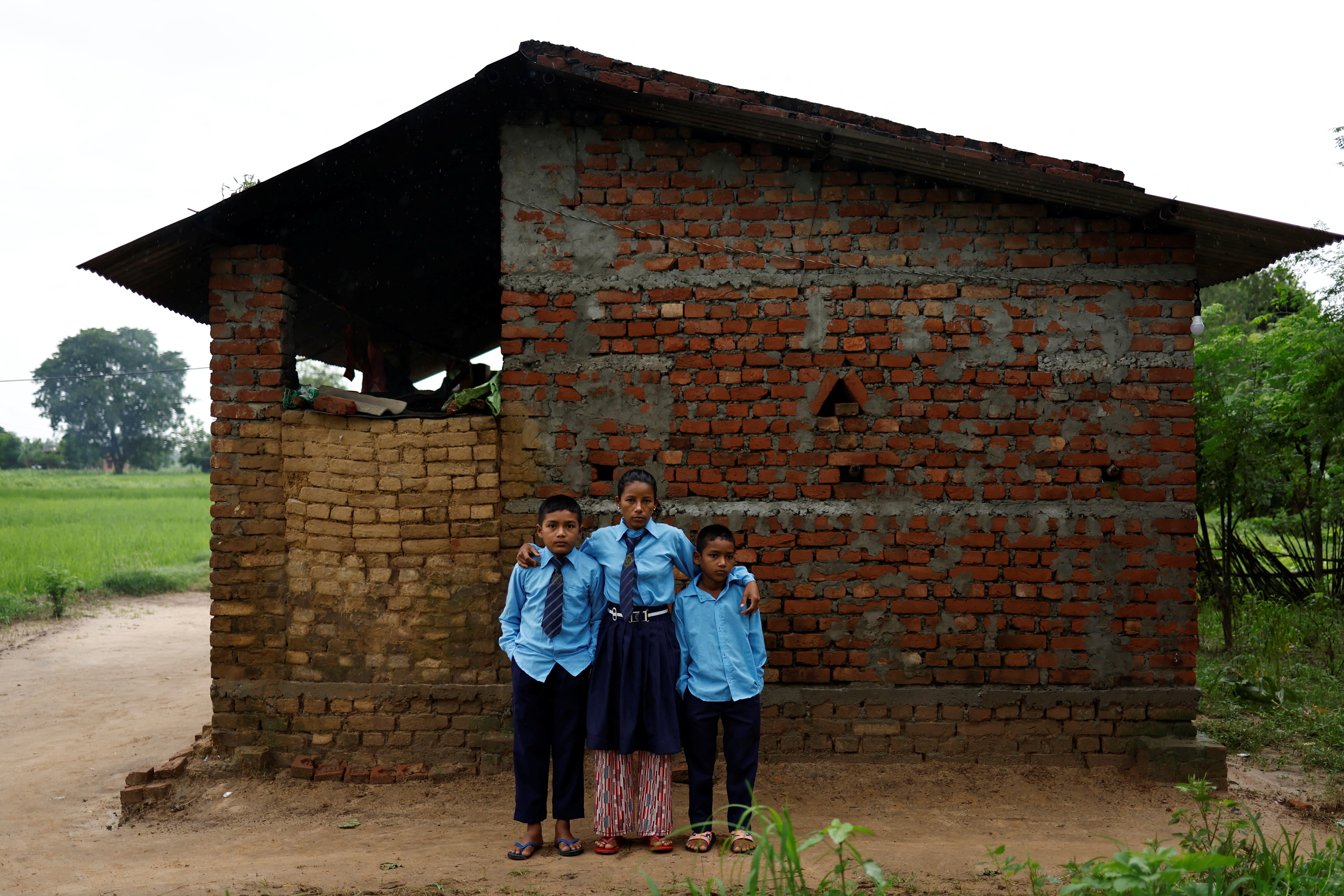 Parwati and her sons, Resham and Arjun, pose outside their house in Punarbas