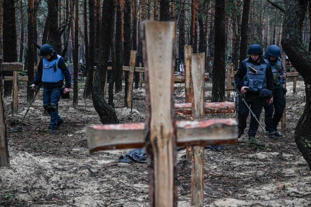 <p>Ukrainian personnel search for landmines at a mass burial site near Izyum on Friday </p>