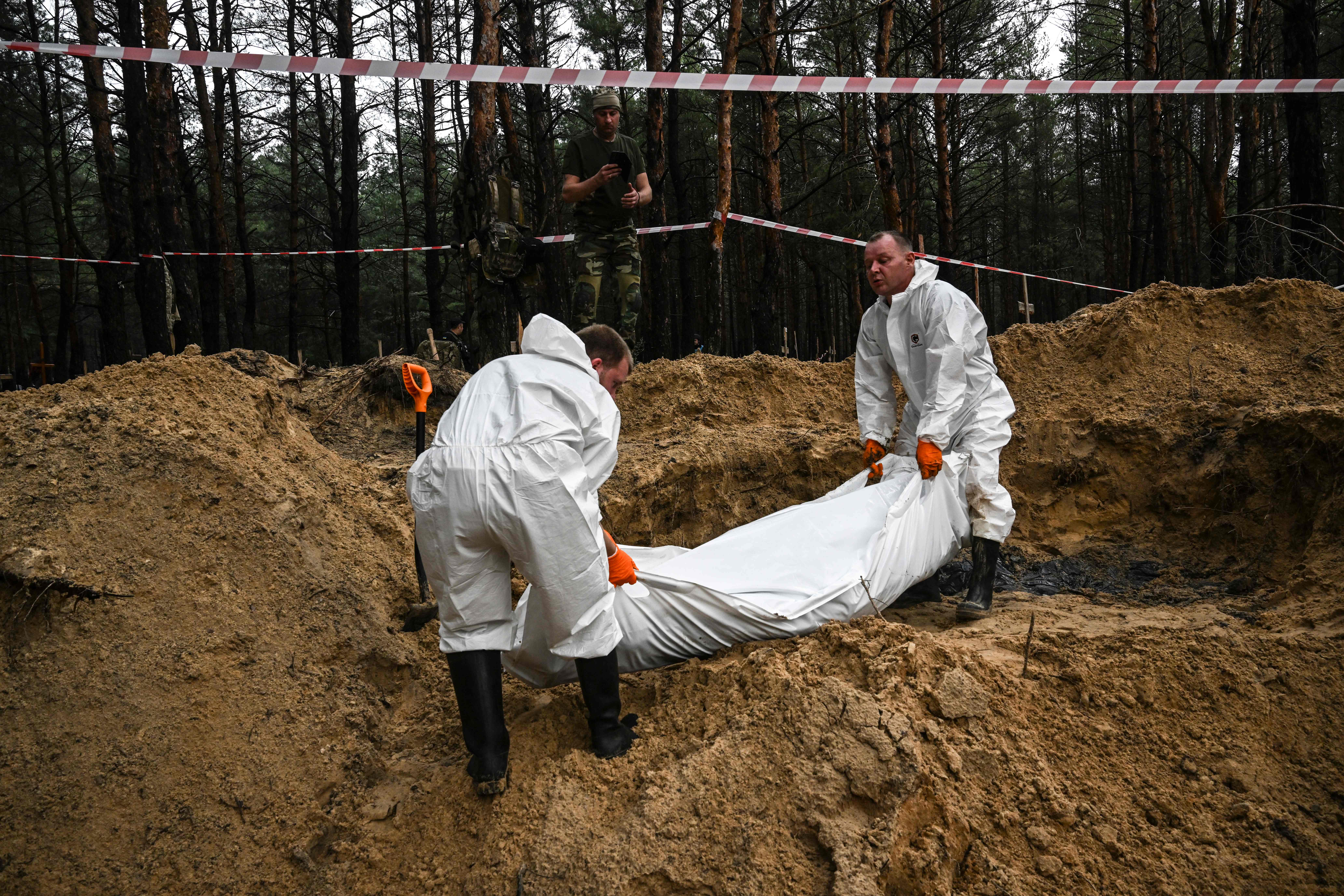 Two forensic technicians carry a body bag in a forest near Izyum on 16 September