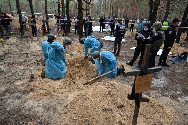 <p>Forensic technicians investigate a grave in a forest on the outskirts of Izyum</p>
