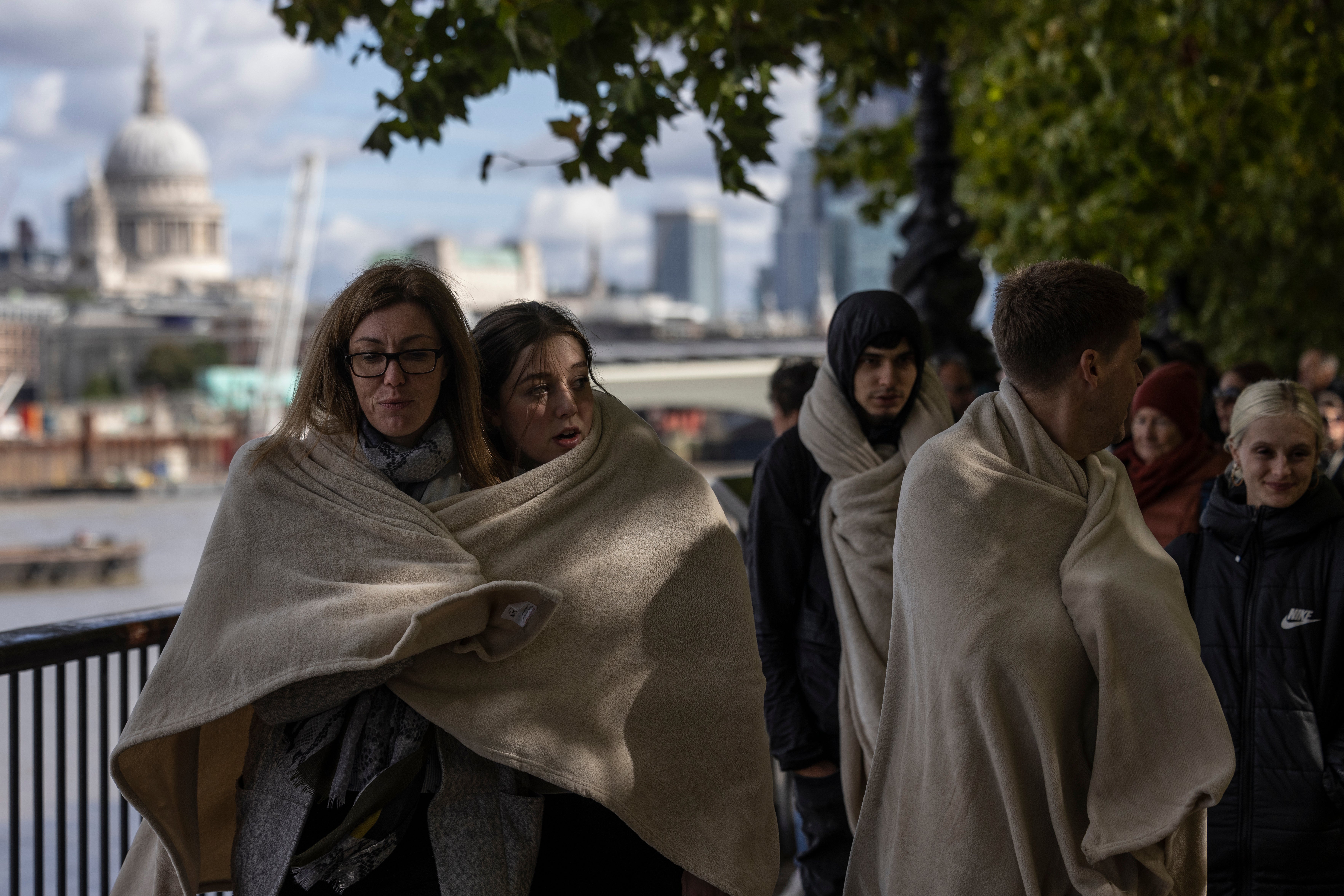 People keep warm by huddling together under blankets as they wait in line to visit Her Majesty’s coffin