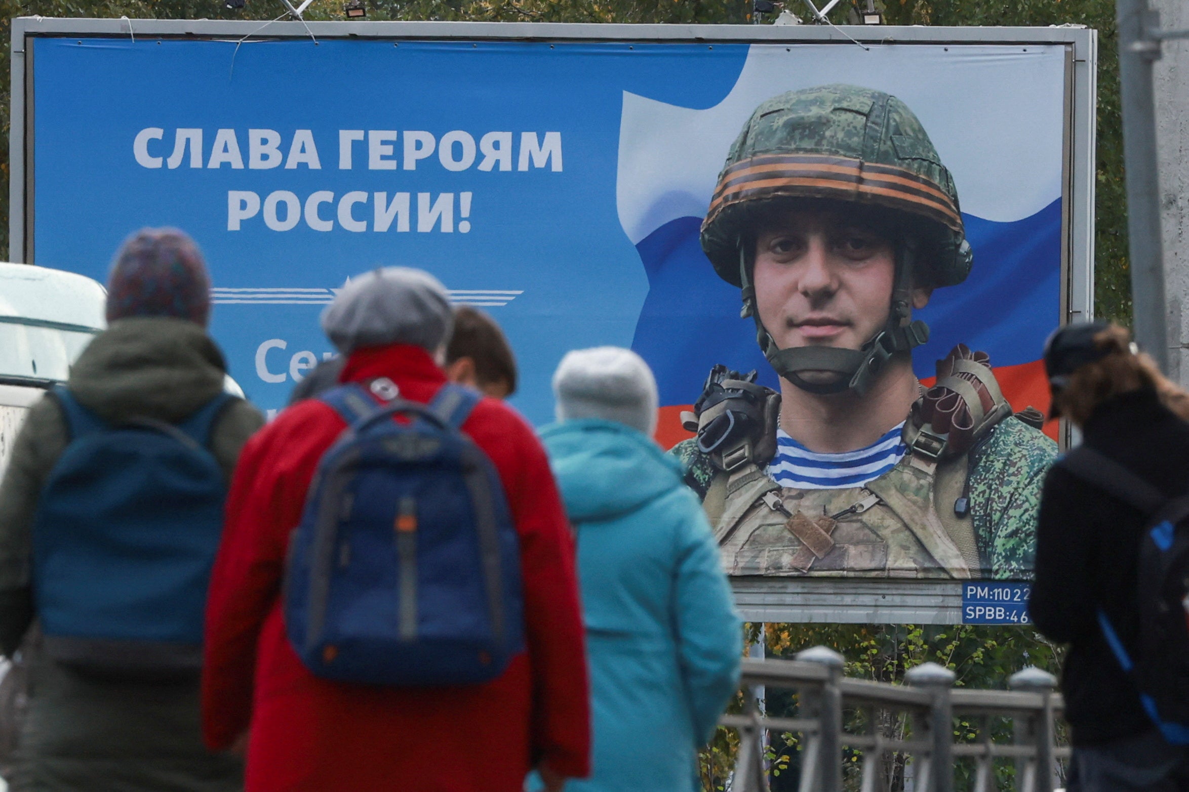 People gather at a tram stop in front of a board displaying a portrait of Russian service member Sergei Tserkovniy in Saint Petersburg, Russia September 21, 2022. A slogan on the board reads: "Glory to heroes of Russia!"