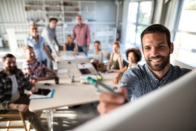 <p>Happy businessman writing a business plan on whiteboard to his team on a meeting in board room.</p>