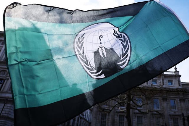 <p>A demonstrator waves an ‘Anonymous’ hacking group flag during a protest in London on 2 April, 2022</p>