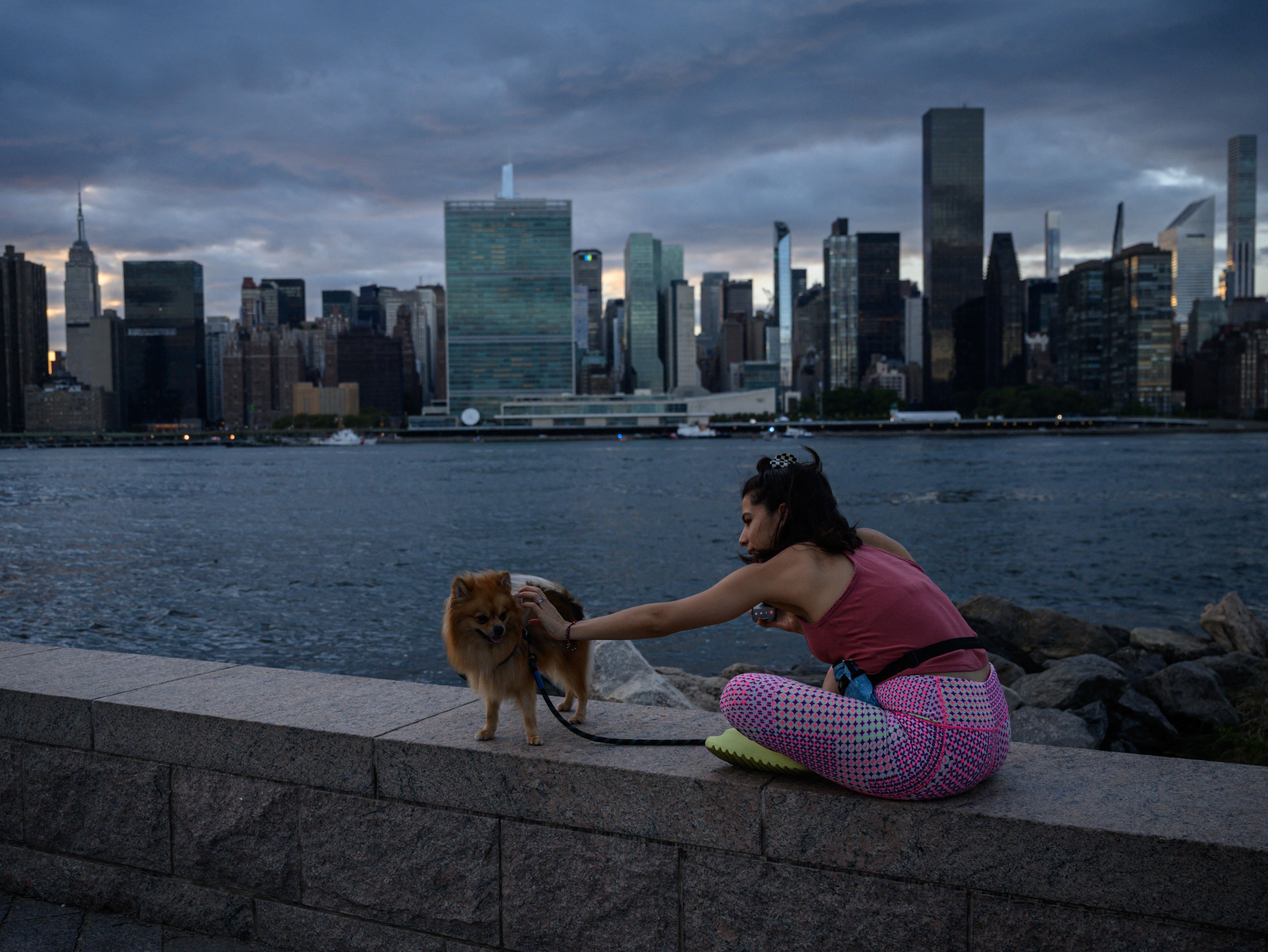 A woman sits with her dog before the UN headquarters building during the 77th session of the United Nations General Assembly