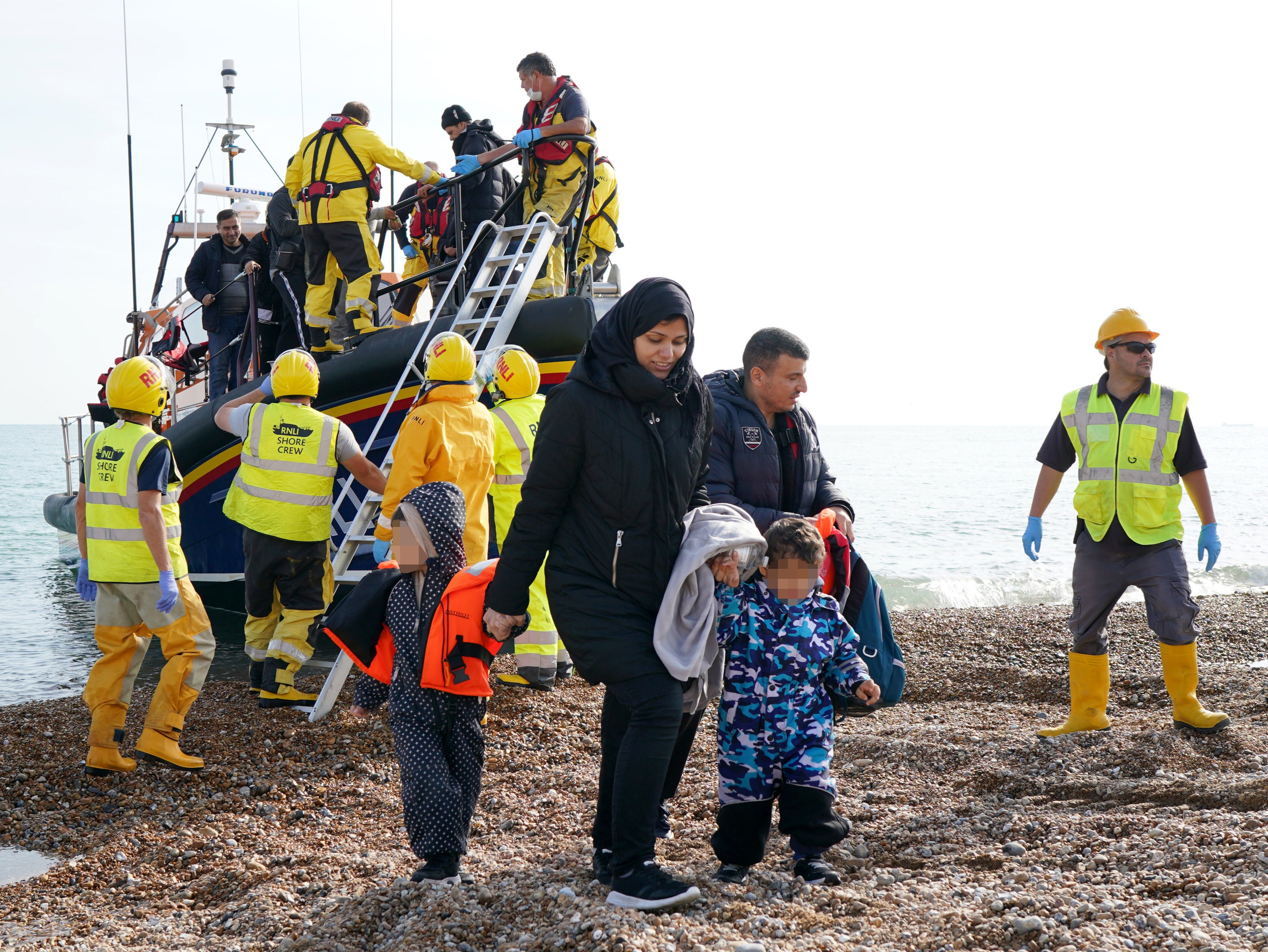 A young family are helped to shore as a group of people thought to be migrants arrive in Dungeness, Kent, after being rescued in the Channel by the RNLI following a small boat incident on Thursday