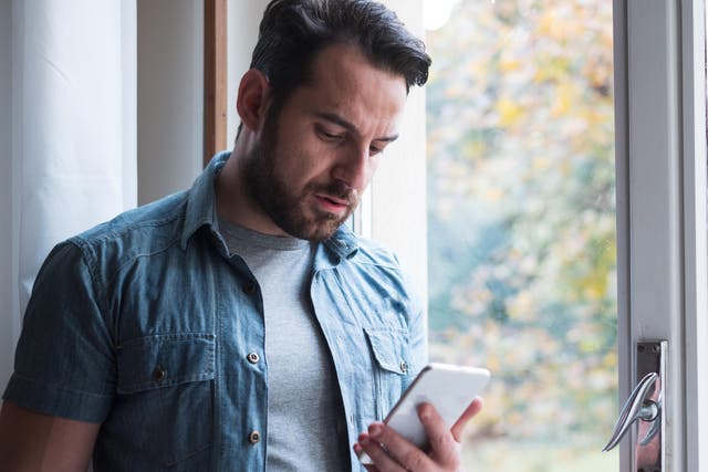 RBXM0M Sad man holding phone alone at home