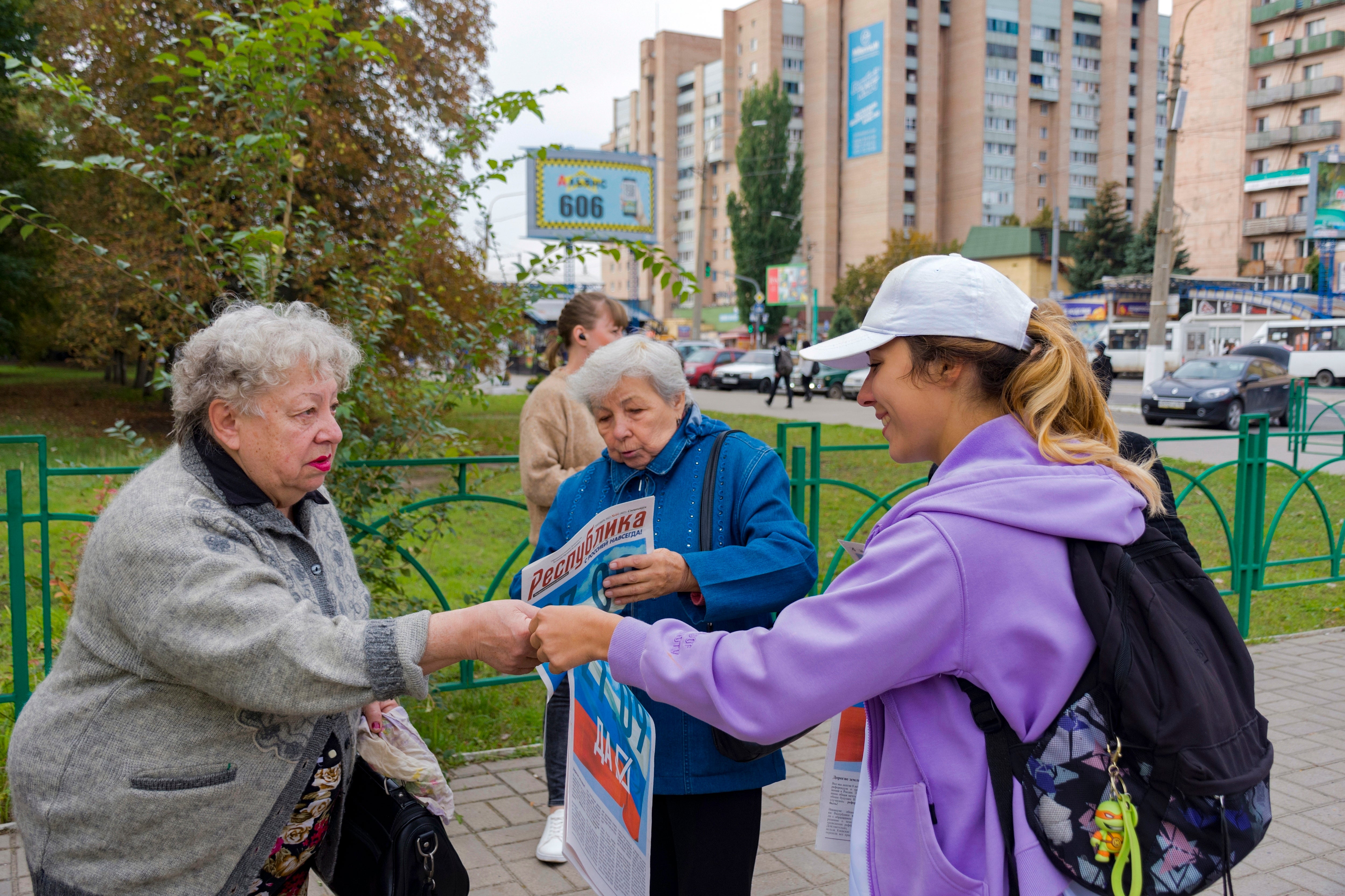 A volunteer for the Luhansk regional election commission, right, distributes newspapers to citizens prior to a referendum in Luhansk