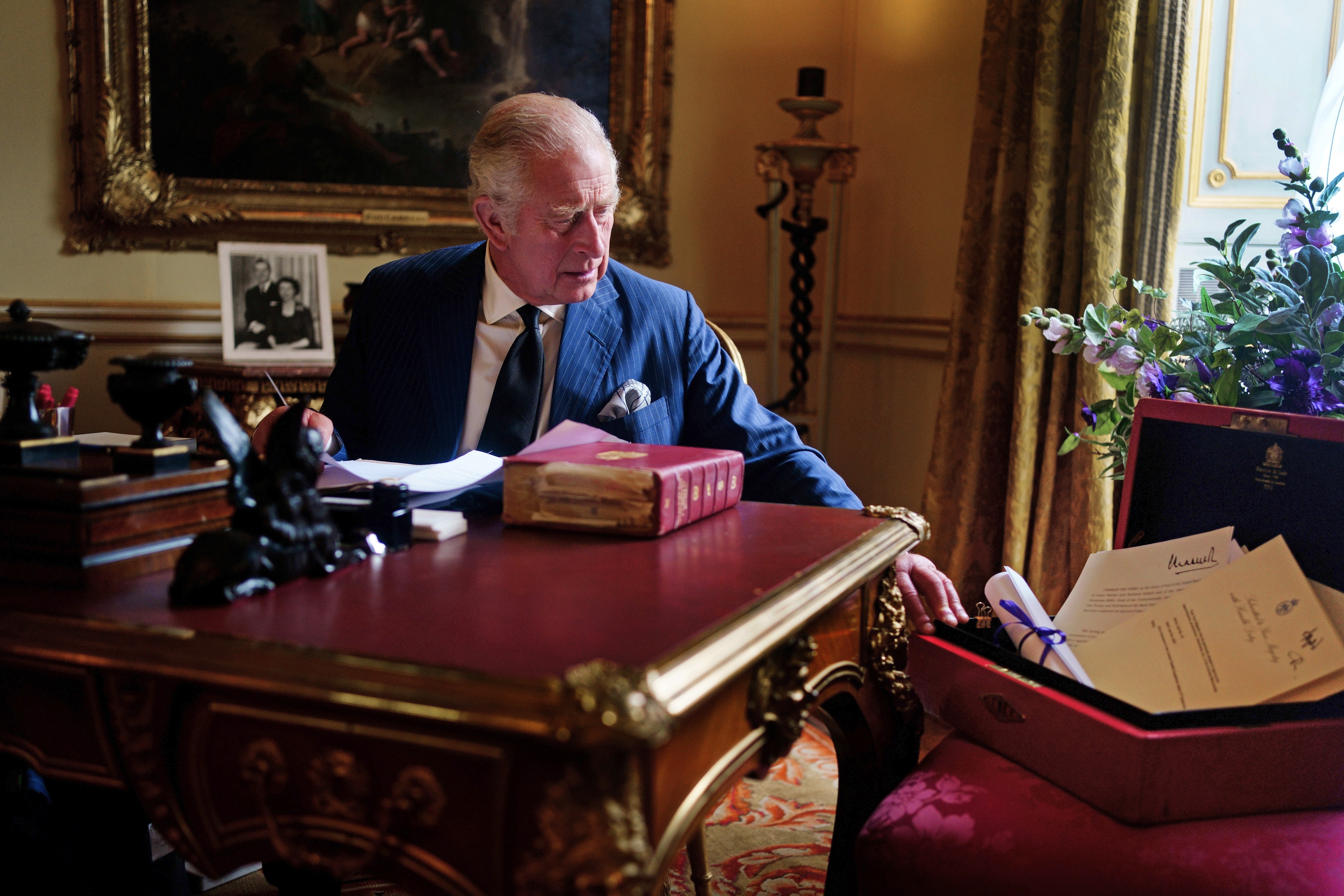 The image shows the King carrying out official government duties at Buckingham Palace