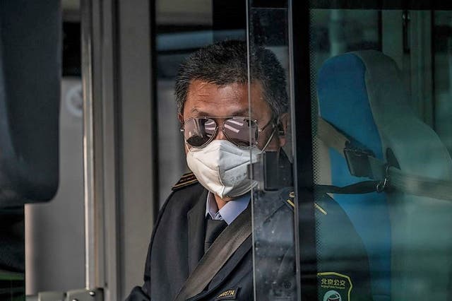 <p>A bus driver wearing a facemask amid the concerns over the Covid-19 coronavirus drives a bus during rush hour on a street in Beijing on 7 April, 2020</p>