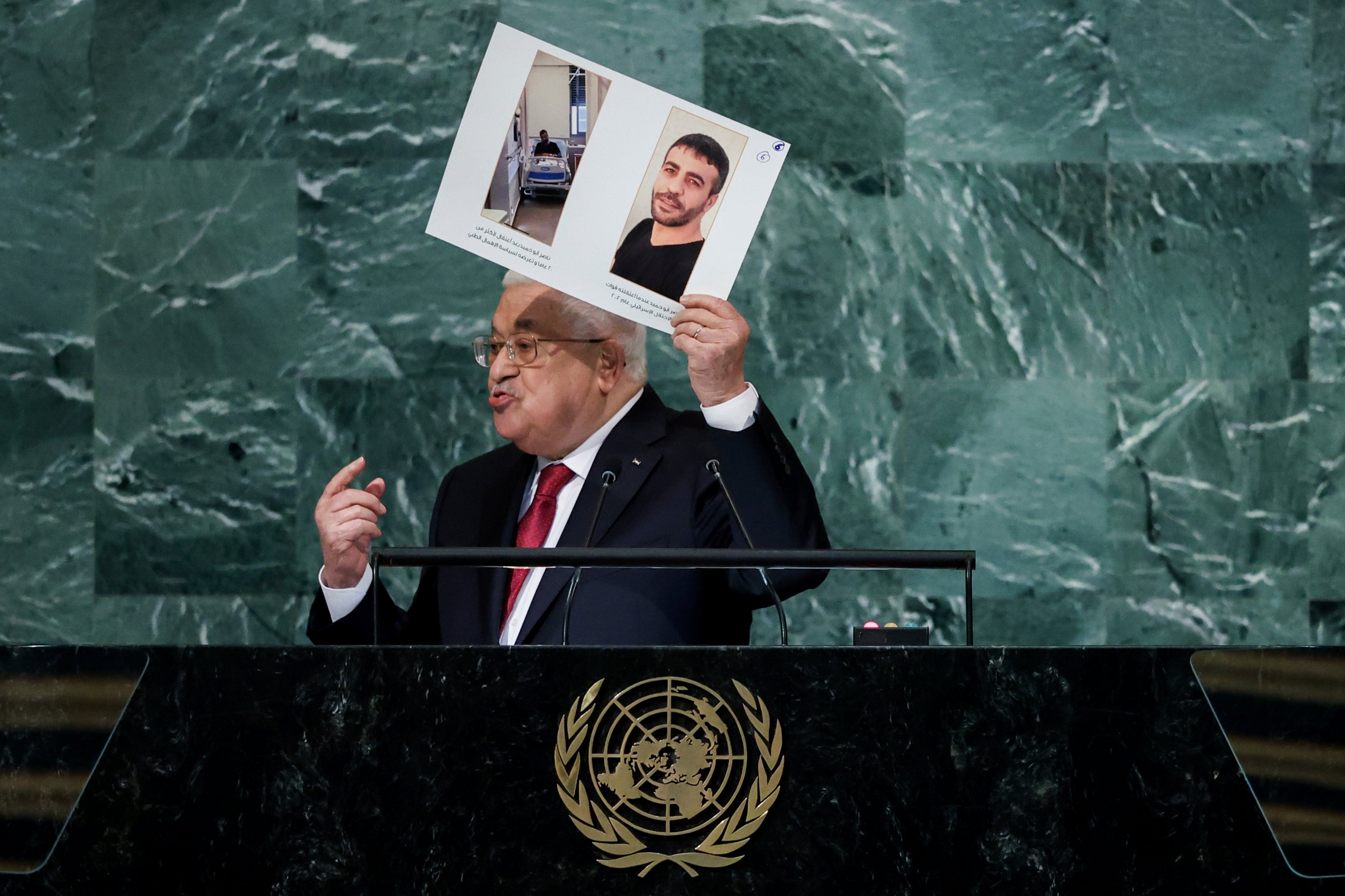 Palestinian President Mahmoud Abbas holds up photographs while addressing the 77th session of the United Nations General Assembl