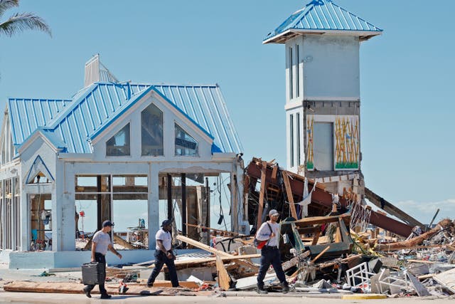 <p>Emergency workers walk past the remains of a clothing store, blown out by Hurricane Ian, in the Times Square area near the Lynn Hall Pier on the island of Fort Myers Beach, Florida, Friday, Sept. 30, 2022. Hurricane Ian made landfall Wednesday, Sept. 28, 2022, as a Category 4 hurricane on the southwest coast of Florida. (Amy Beth Bennett/South Florida Sun-Sentinel via AP)</p>