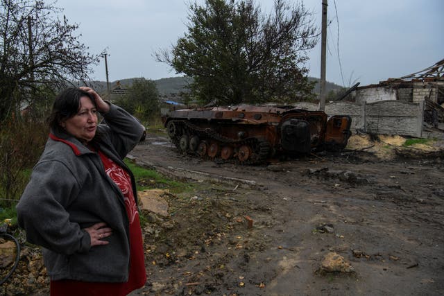 <p>A woman next to a destroyed armoured fighting vehicle in the liberated Ukrainian village of Kamianka</p>