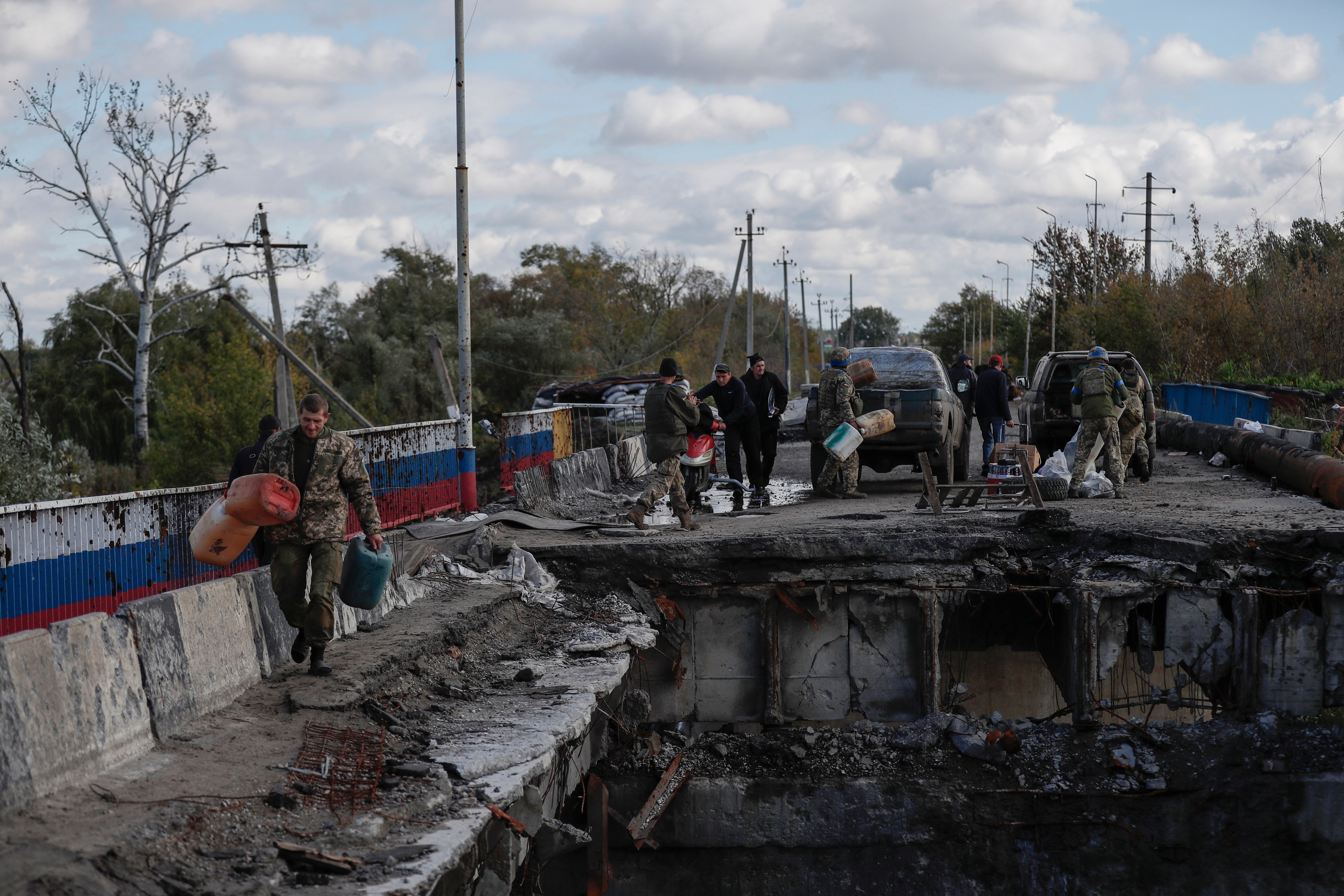 Ukrainian soldiers carrying supplies across a damaged bridge into the newly liberated city of Kupyansk, east of Kharkiv
