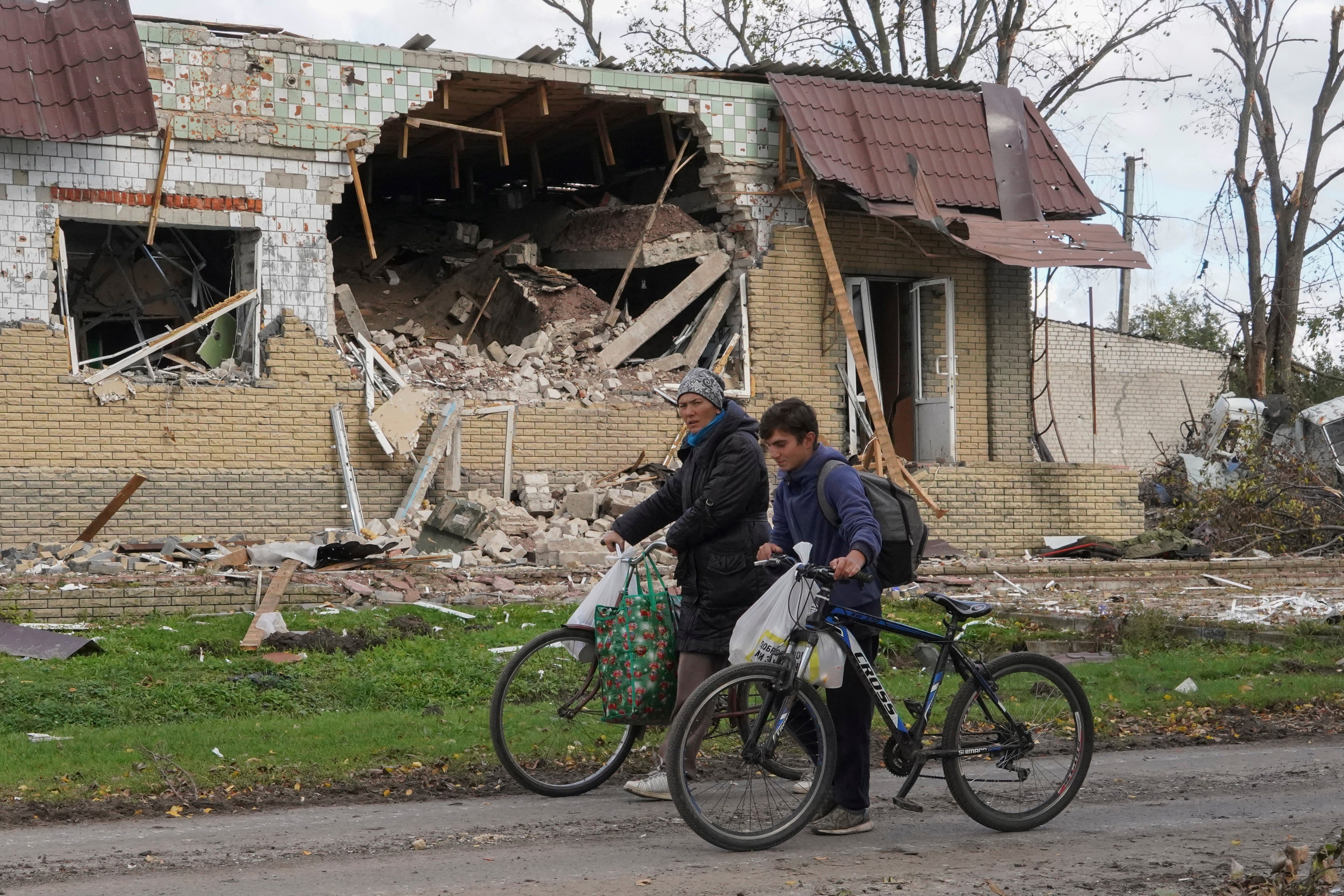 Locals walks with bicycles in front of a damaged cafe in the recently recaptured village of Petropavlivka