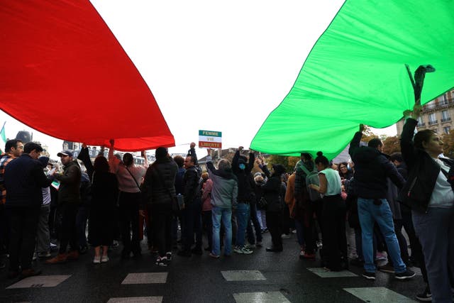 Protesters stand under an Iranian flag during a demonstration to show support for Iranian protesters standing up to their leadership over the death of a young woman in police custody in Paris (Aurelien Morissard/AP)