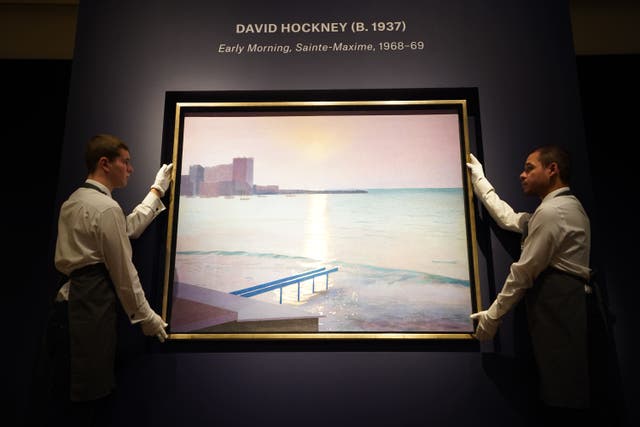 Art handlers holding David Hockney’s, Early Morning, Sainte-Maxime, during a photo call for highlights from Christie’s forthcoming evening sales, their 20th/21st Century and A Place With No Name: Works from the Sina Jina Collection sales, at Christie’s in London (James Manning/PA)