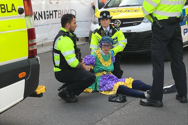 <p>A protestor in fancy dress surrounded by police officers</p>