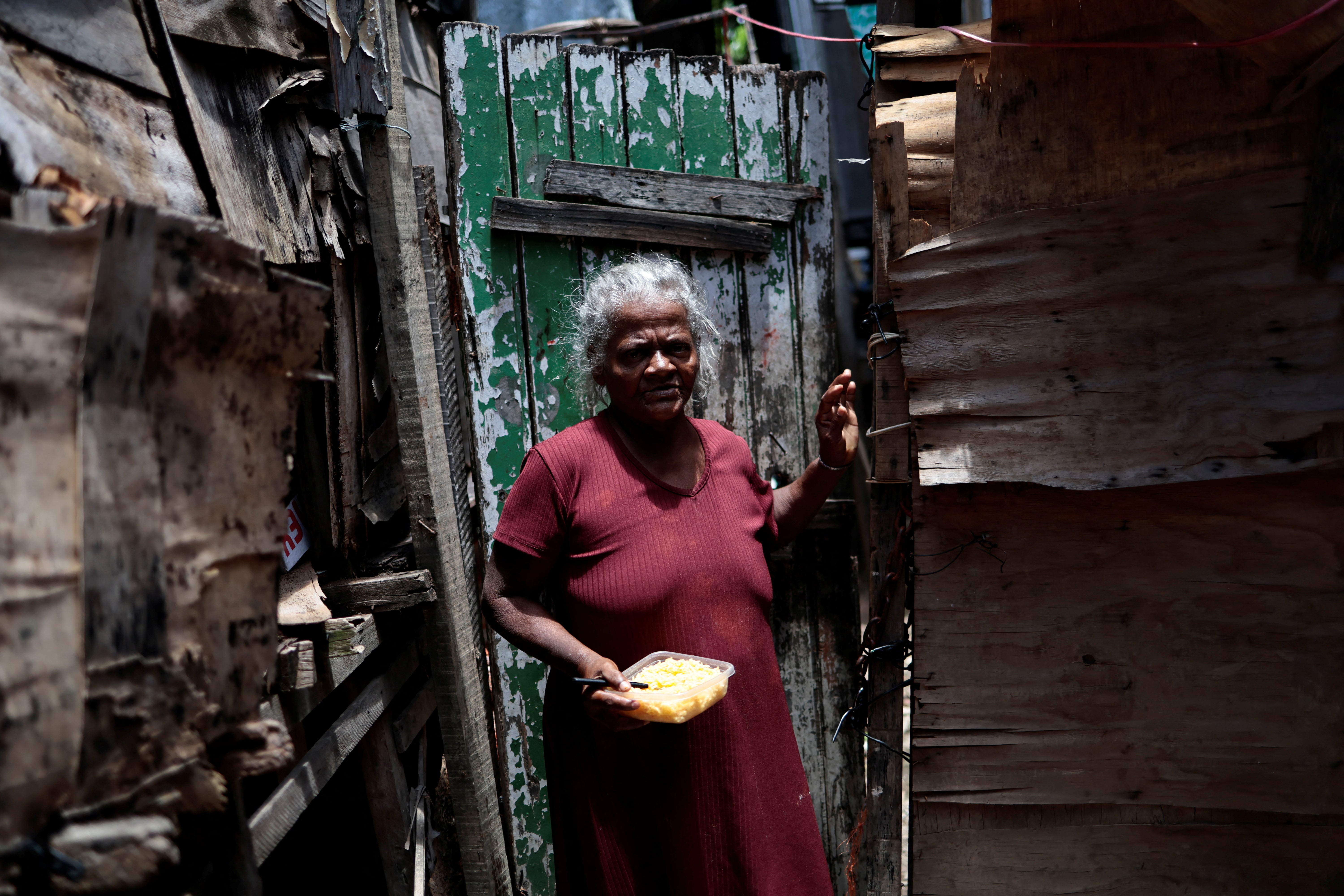 Maria Jose holds her lunch, a bowl of rice, in front of her house in the Arco Iris favela